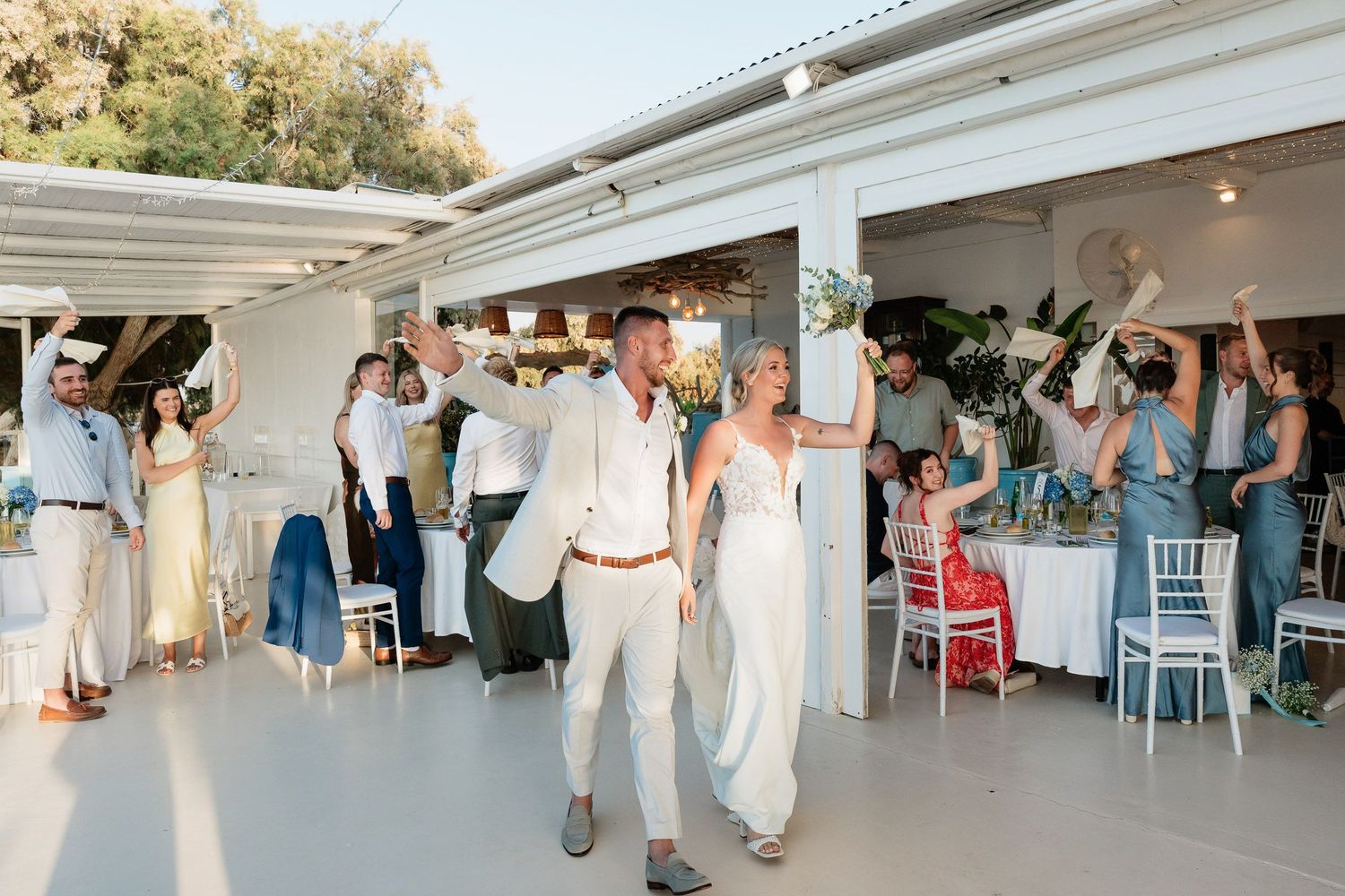 Wedding guests dance together on an outdoor patio venue during a festive celebration at sunset.