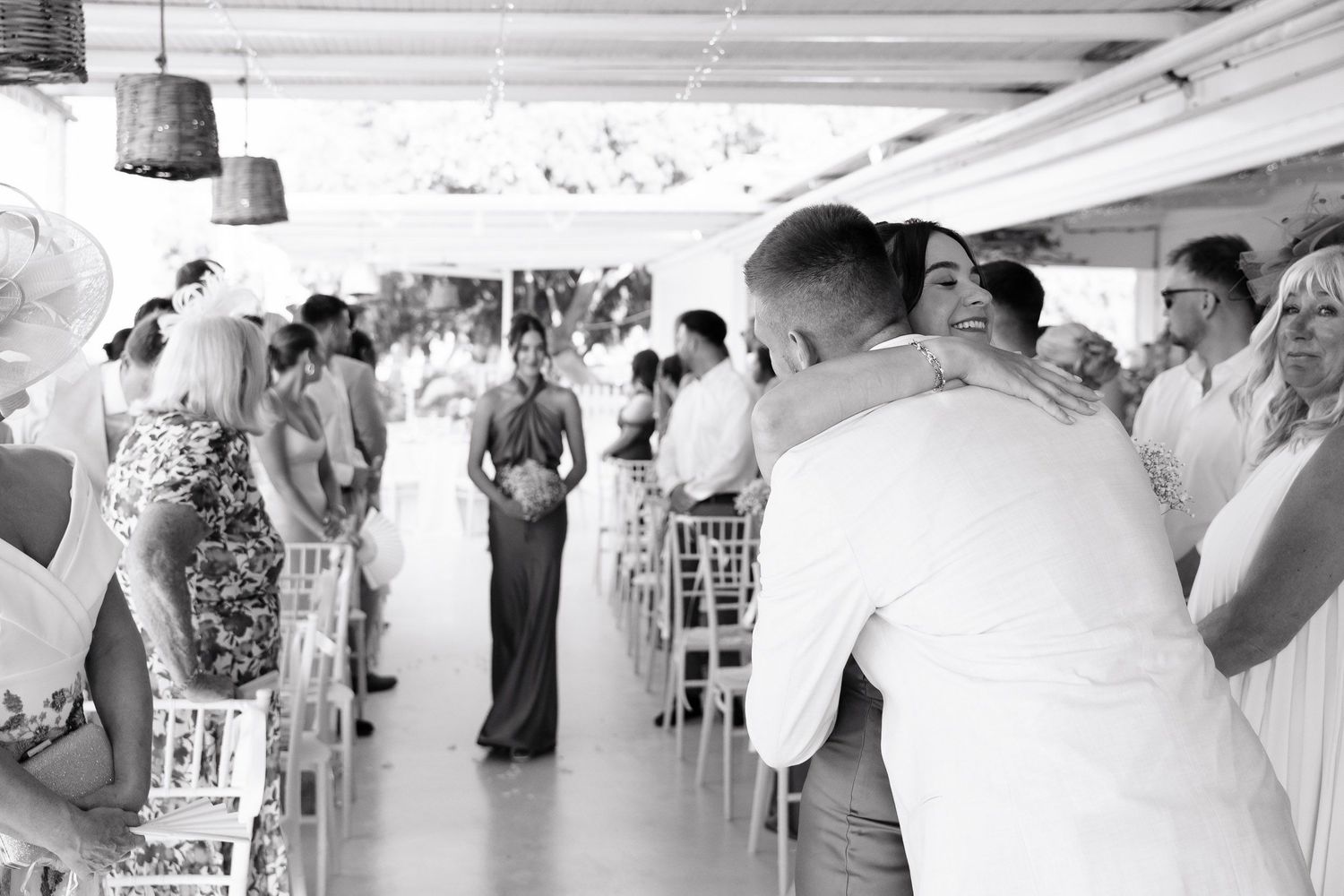 Black and white photo of a wedding ceremony taking place under a covered outdoor venue with guests seated in rows.