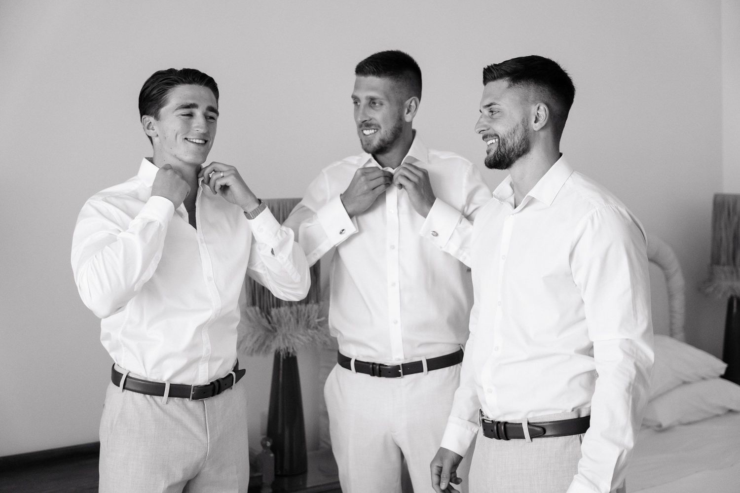 A series of black and white photos showing groomsmen in white shirts and dark belts laughing and joking together.