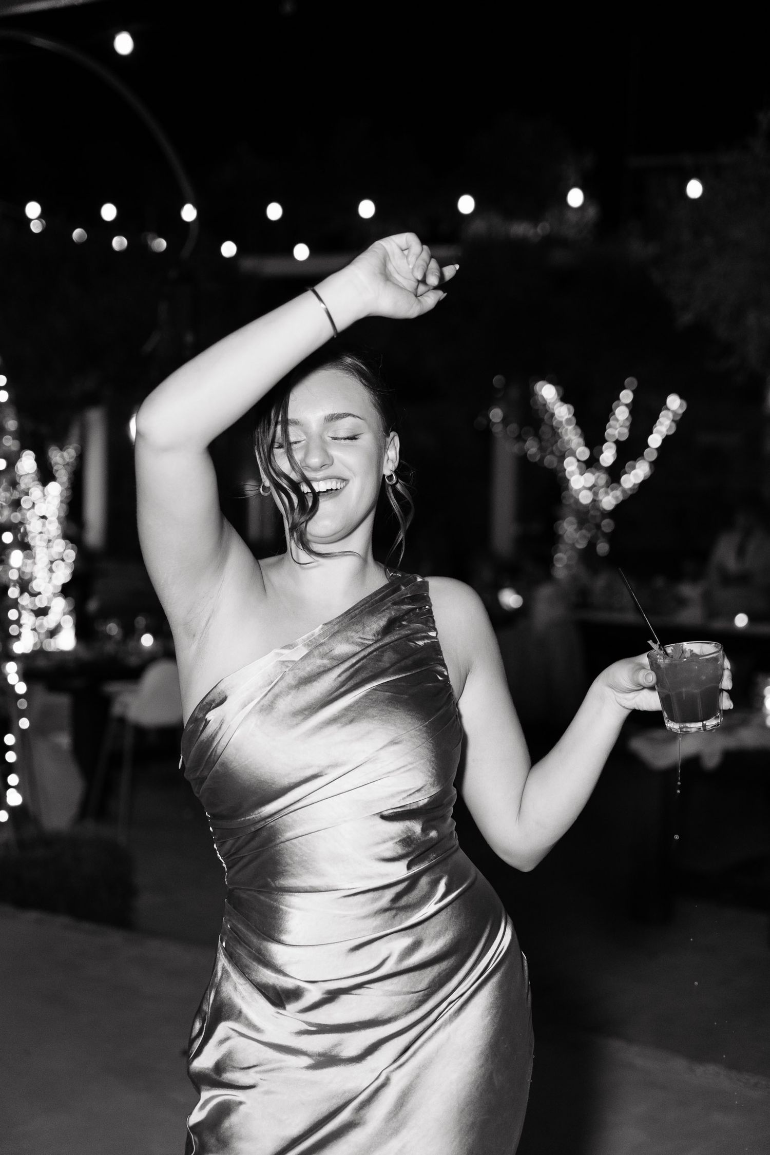 A person in a shiny silver dress dances energetically in a series of black and white photos with twinkling lights in background.