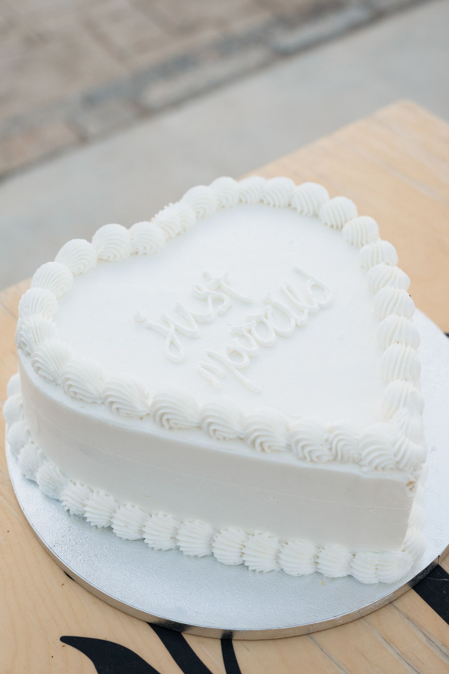 A heart-shaped white wedding cake with delicate piped frosting details on a wooden table.