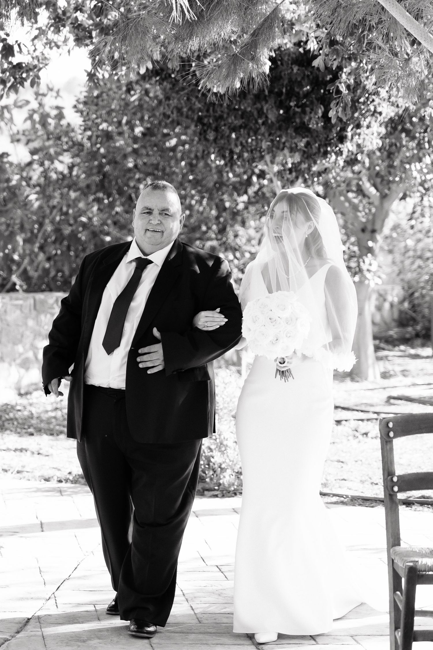 Black and white wedding photos show a couple in formal attire posing together outdoors under trees on their special day.