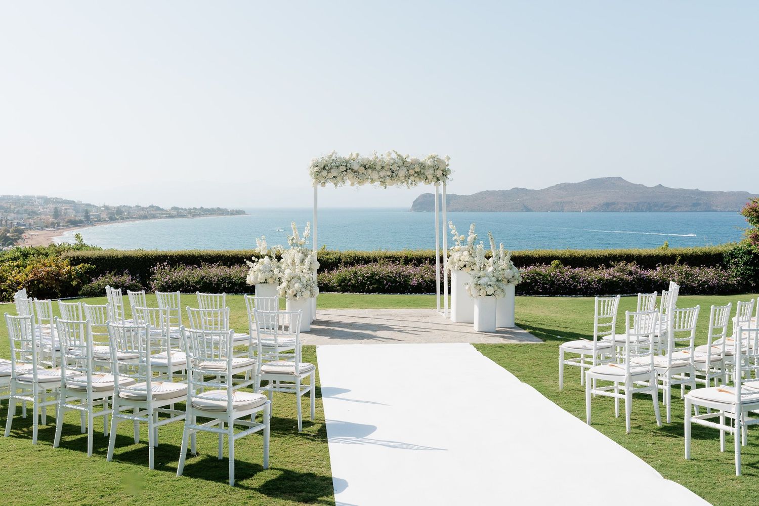 White chairs arranged in rows for an outdoor wedding ceremony with scenic mountain and ocean views in the background.