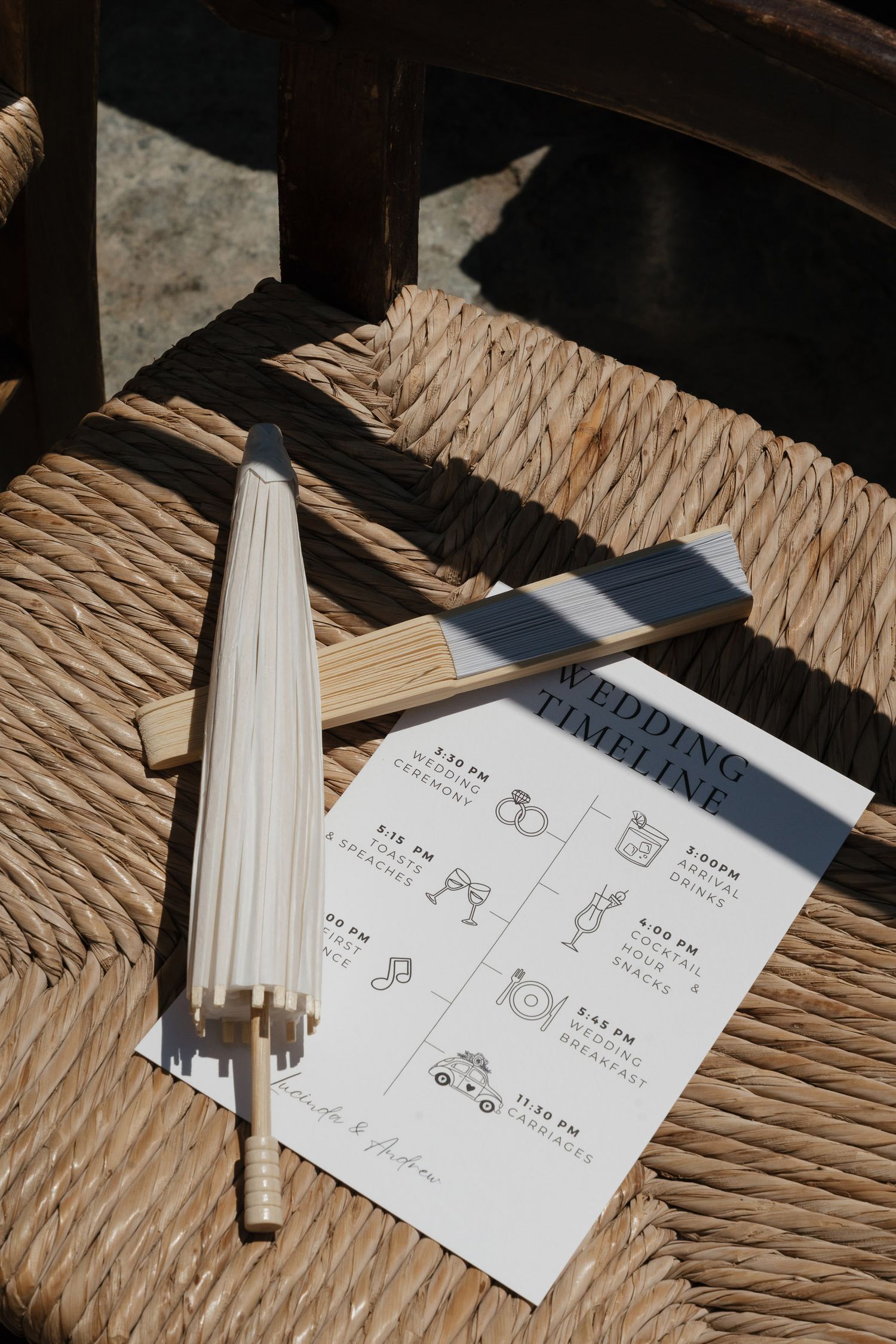A white paper with hand-drawn icons and instructions sits on a woven chair seat next to an umbrella in natural lighting.