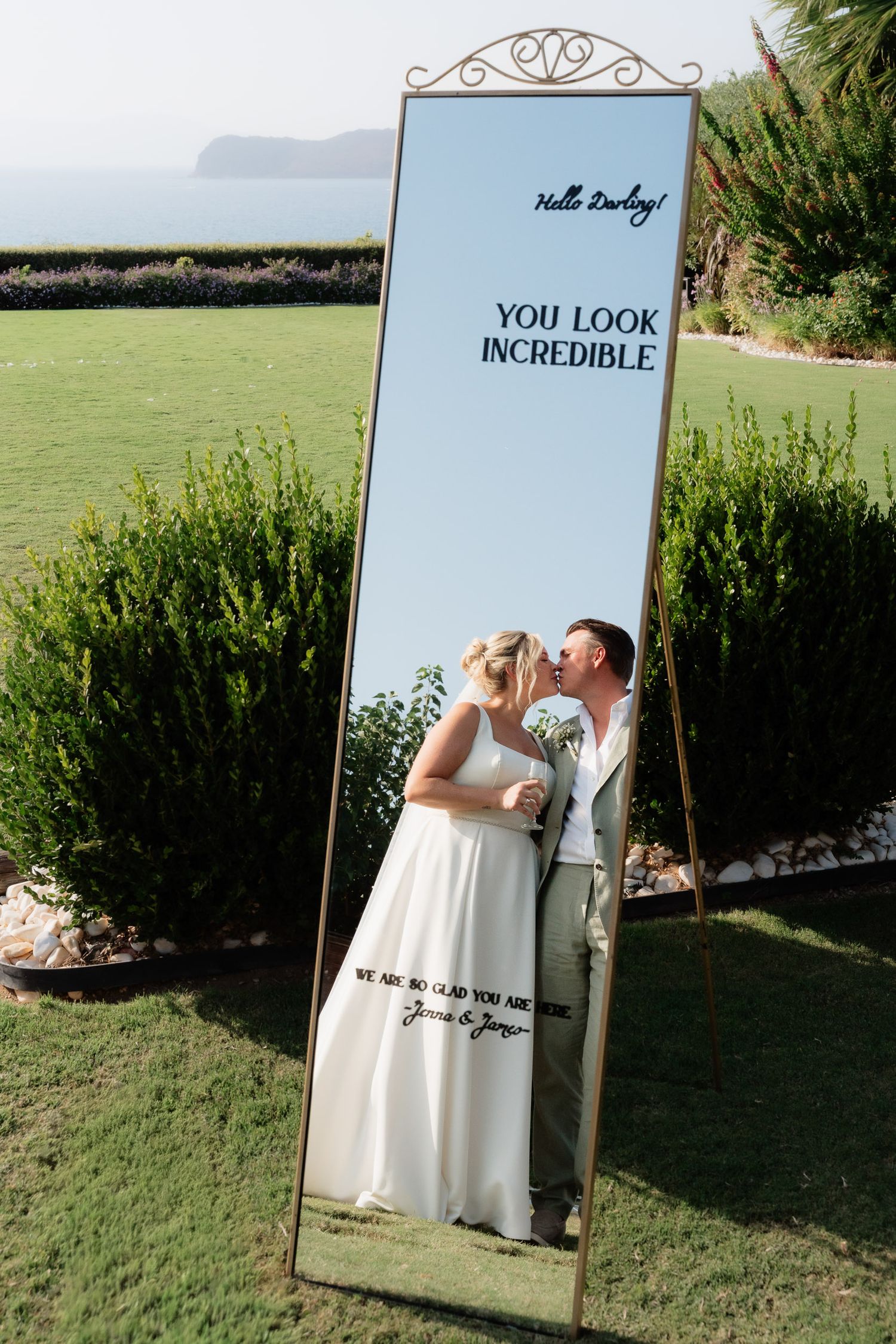 A creative wedding photo series showing reflections in multiple mirrors placed outdoors on grass with hedges.