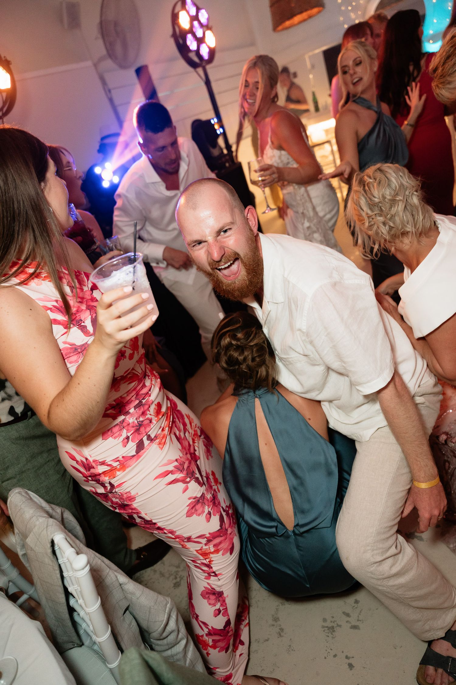 Party guests dancing and celebrating on a dance floor with vibrant lighting and festive atmosphere.