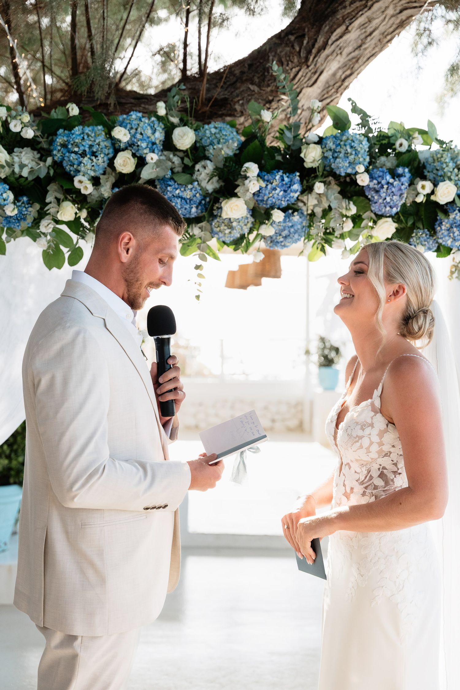 A couple exchanges vows under an elegant floral arch decorated with blue hydrangeas and white flowers at their wedding ceremony.