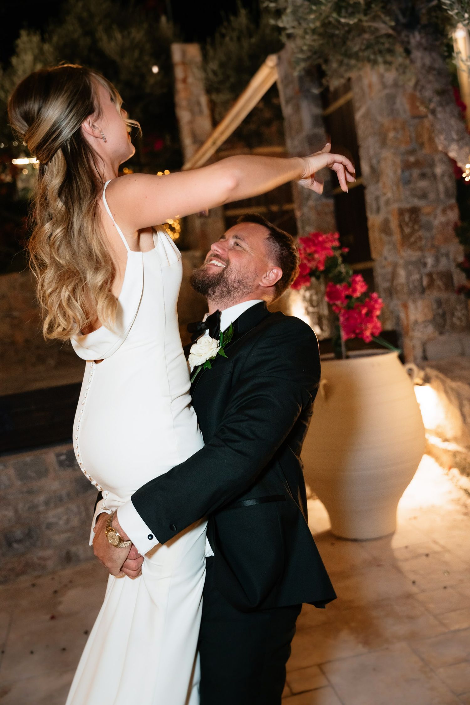 A newlywed couple shares a romantic dance sequence in a rustic indoor venue with stone walls and soft lighting.