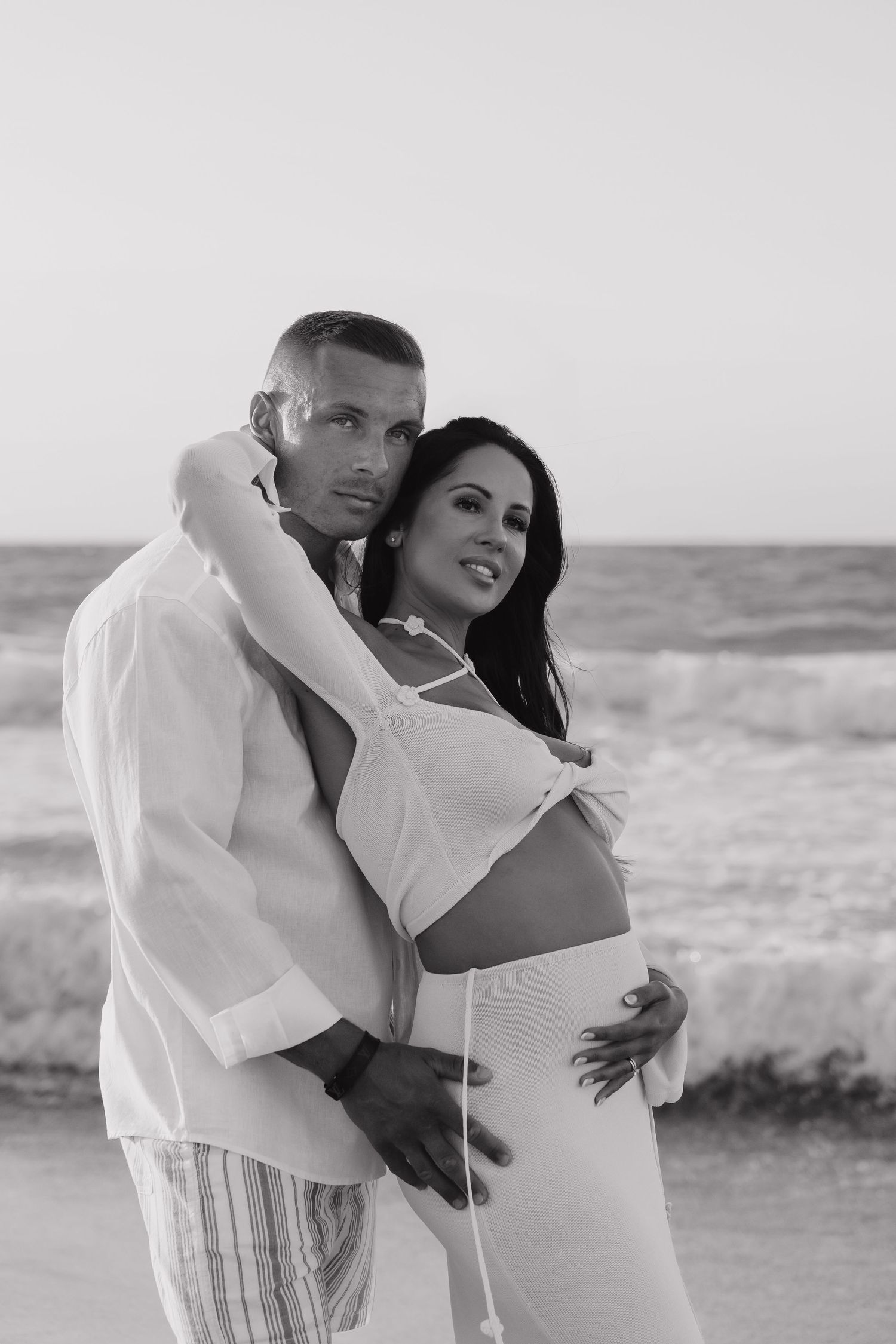 A romantic black and white photo series showing a couple embracing on a beach with ocean waves in the background.