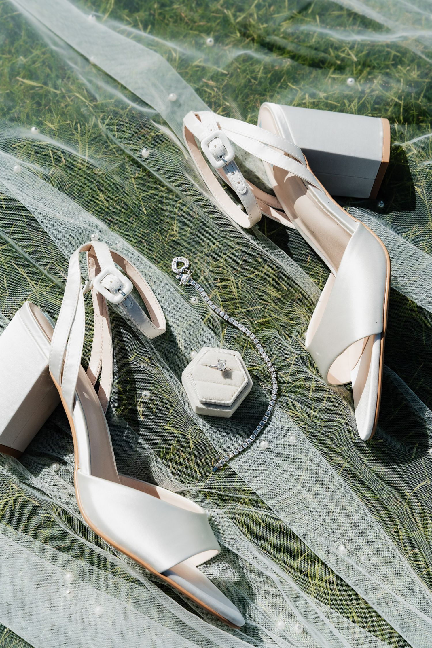 Elegant white slingback wedding shoes with block heels displayed with a hexagonal ring box on a reflective surface.