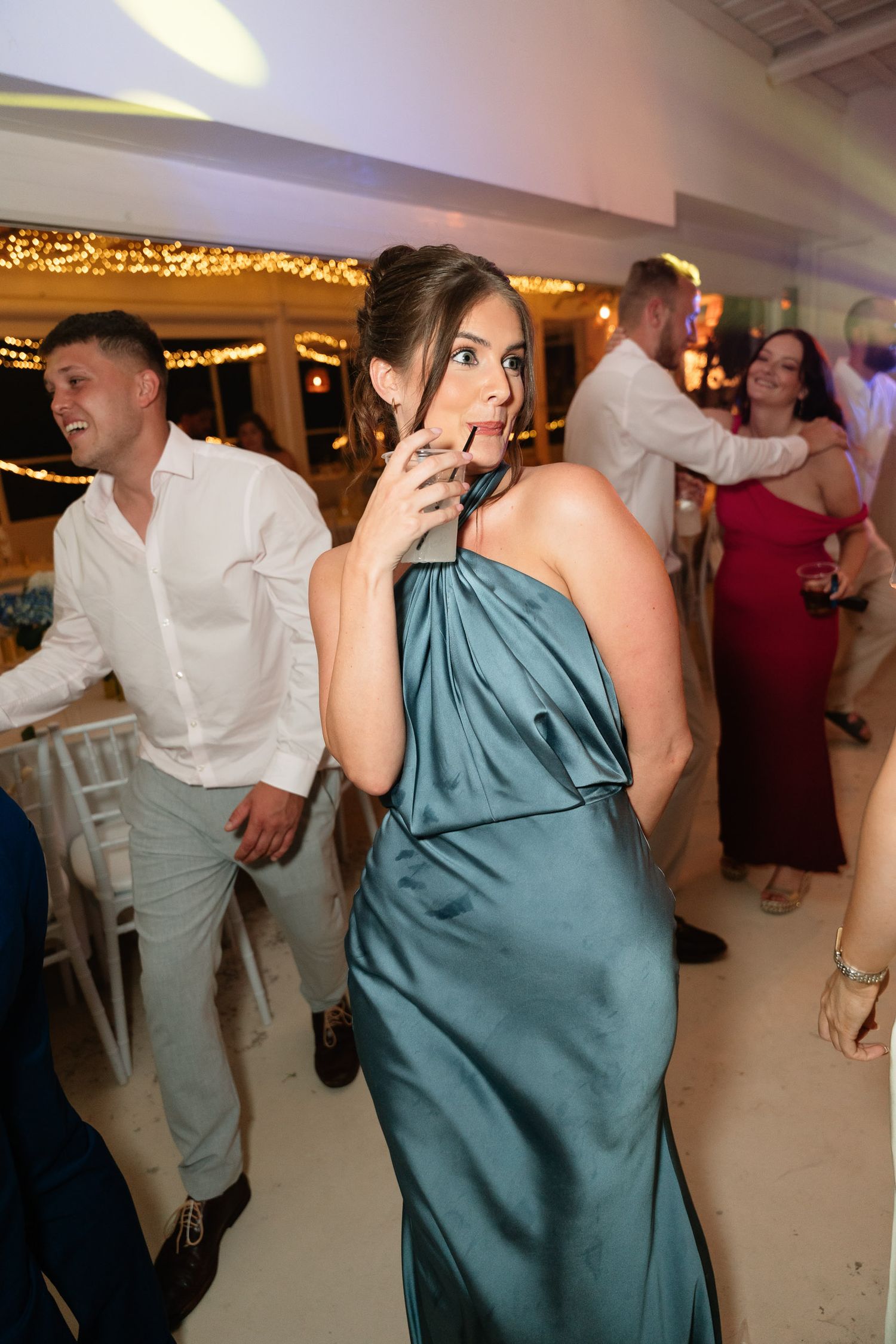 Couples dancing and enjoying themselves at a wedding reception with string lights and white walls in the background.