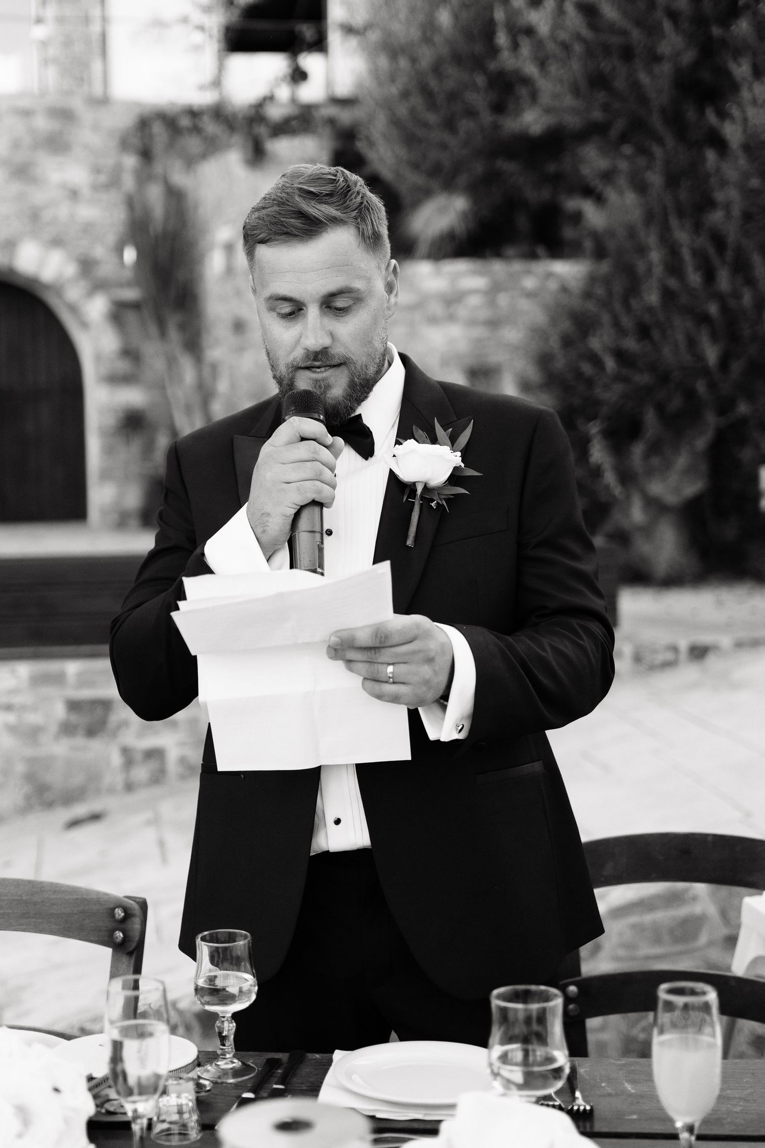 A man in a black tuxedo becomes emotional while reading a letter at a formal dining table.
