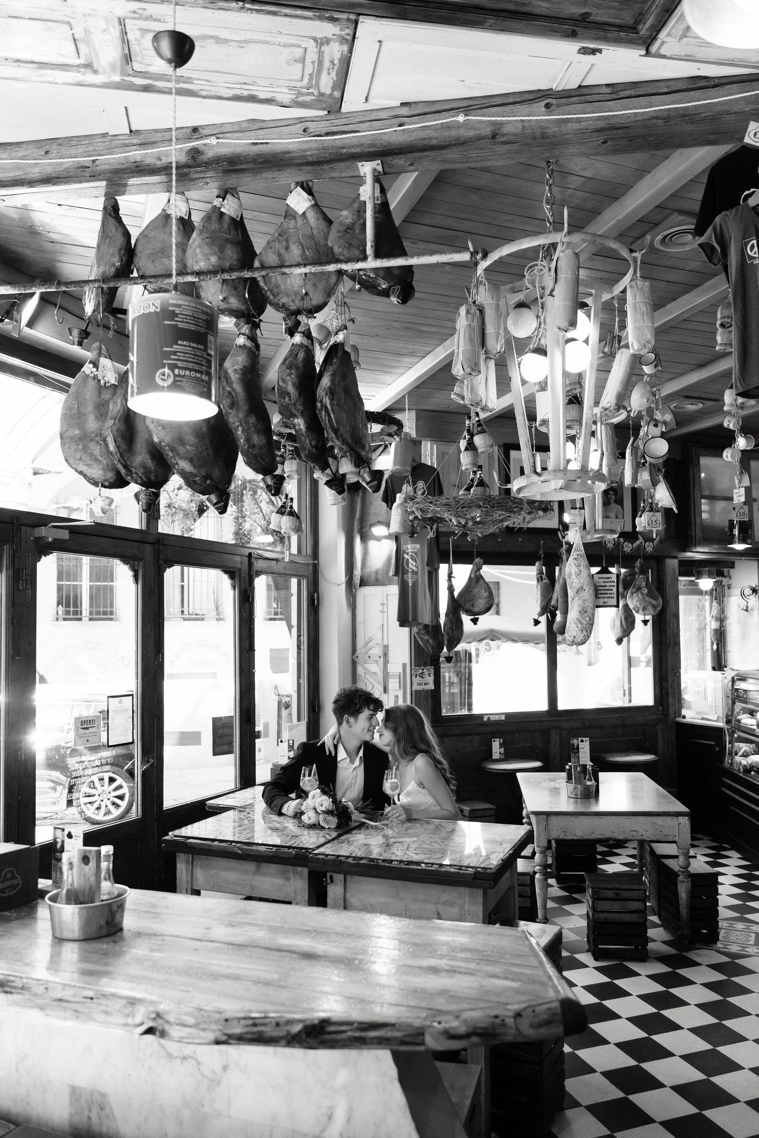 Couple dining in rustic charcuterie restaurant with cured meats hanging from ceiling, black and white photo.