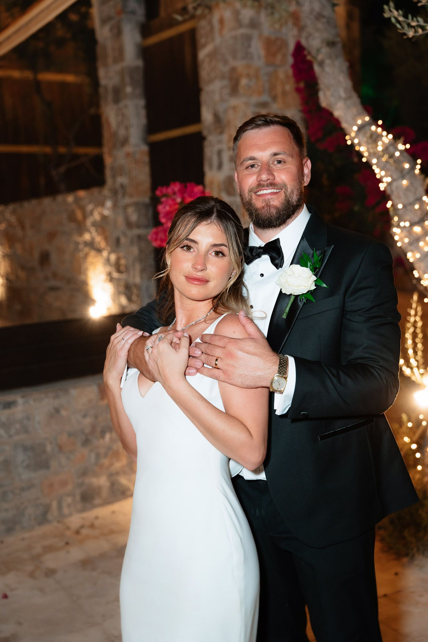 A couple shares a romantic dance moment in a rustic stone venue decorated with twinkling lights and flowers.