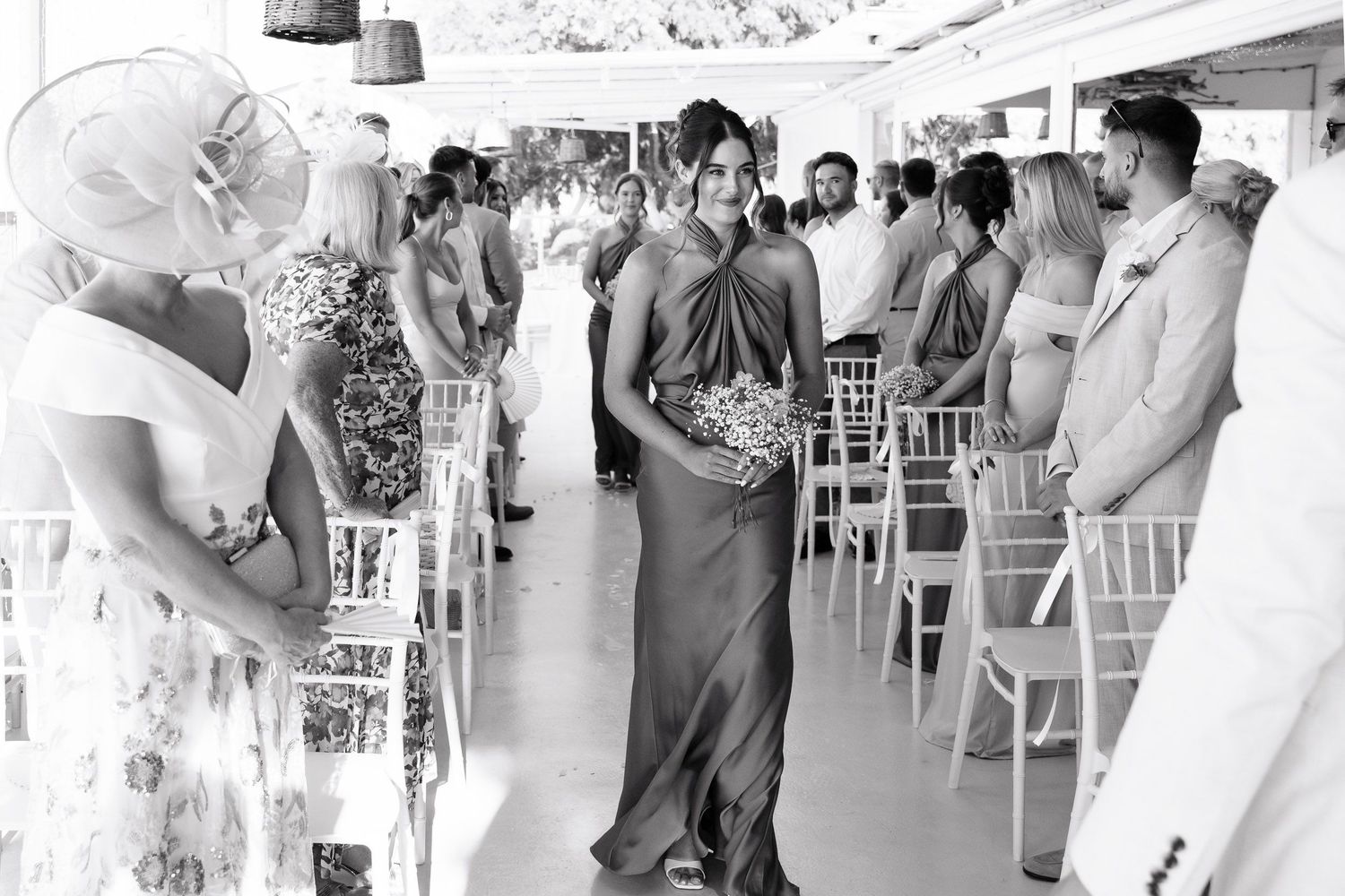 Black and white photo of guests mingling at an elegant outdoor wedding reception with white chairs and decorations.