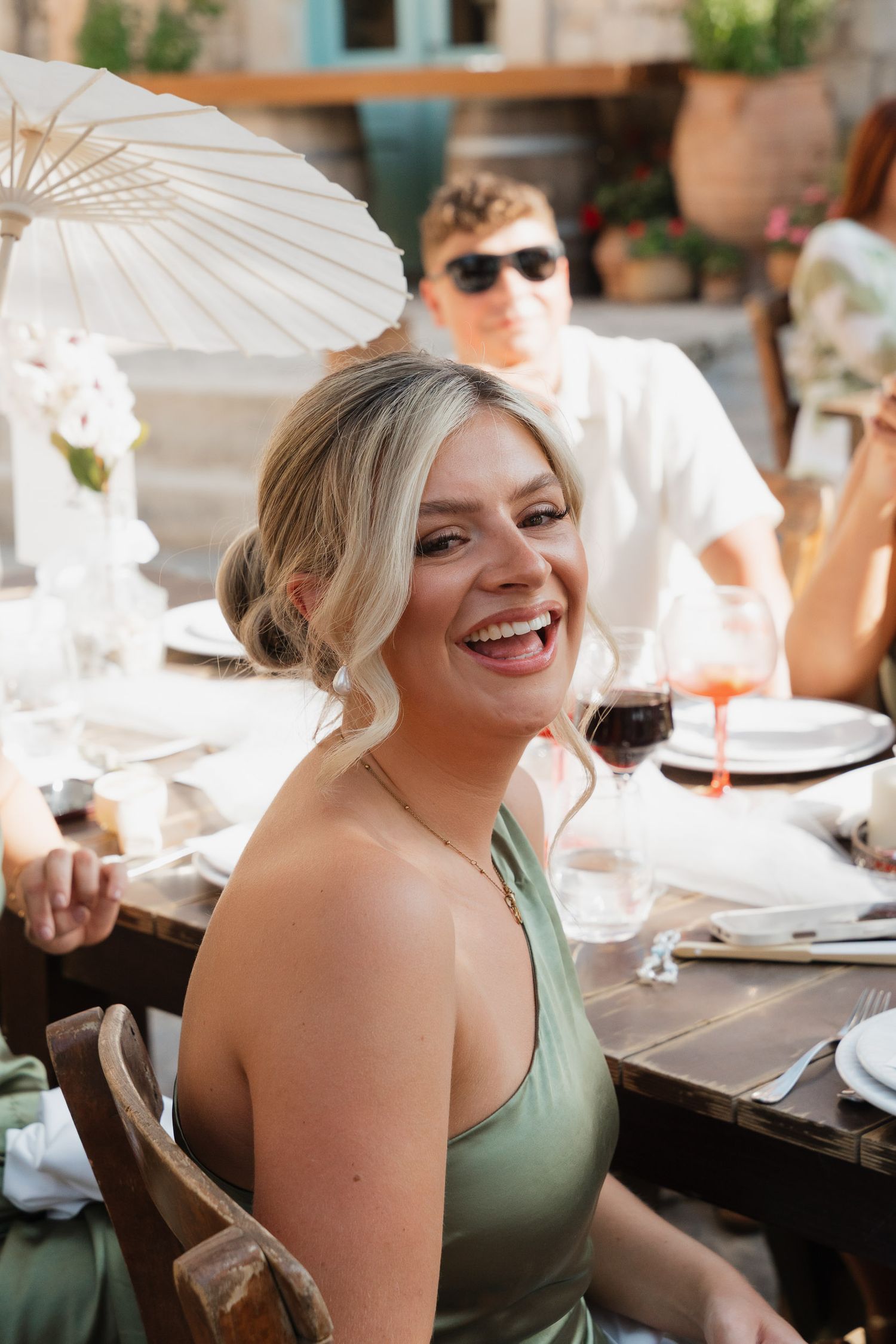 People enjoying an outdoor dining event with a white parasol and wine glasses on a sunny day.