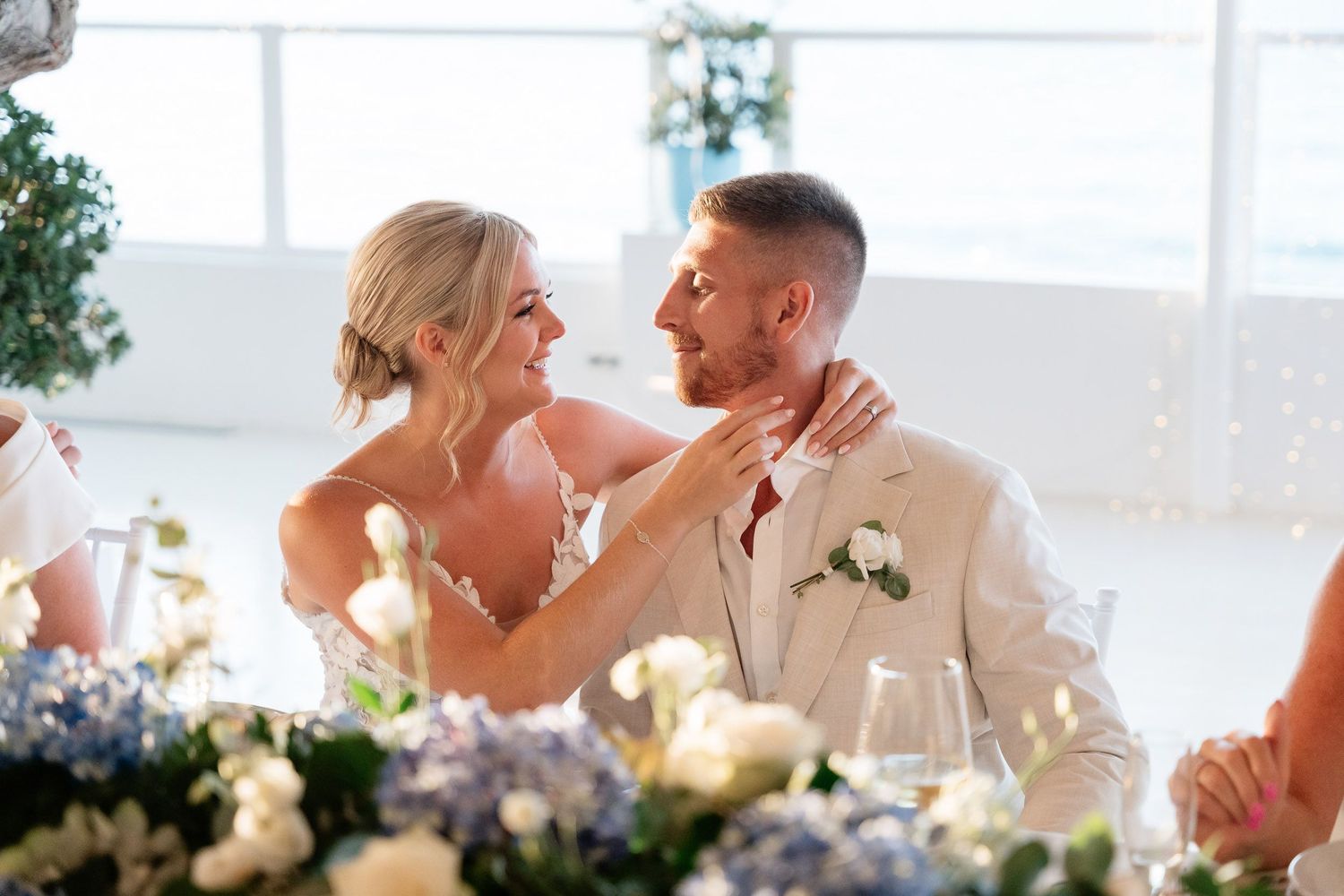 A couple shares a romantic moment on their wedding day in a bright, sunlit room with elegant decor.