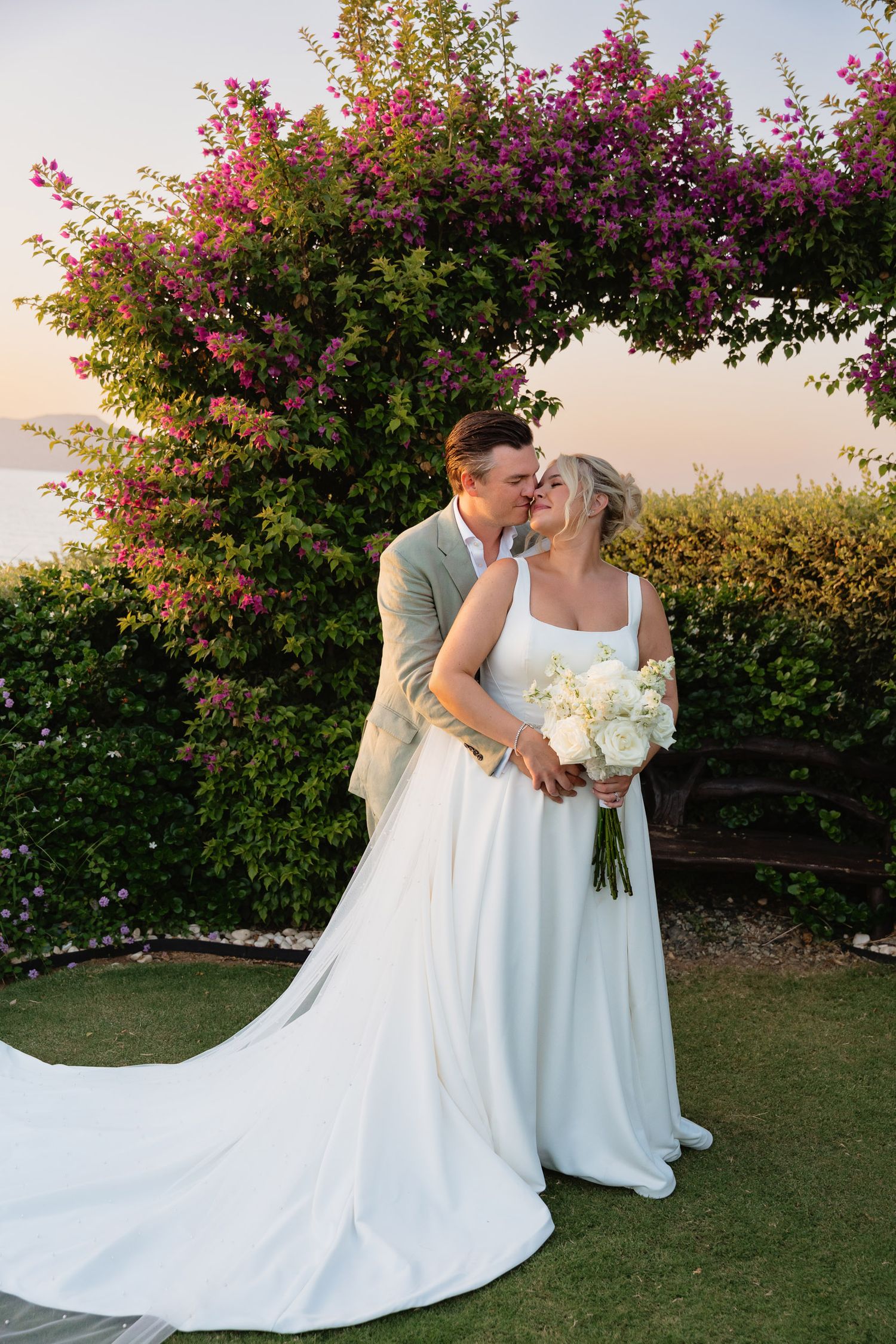 A couple shares a romantic kiss in front of blooming pink bougainvillea during their outdoor wedding photoshoot.
