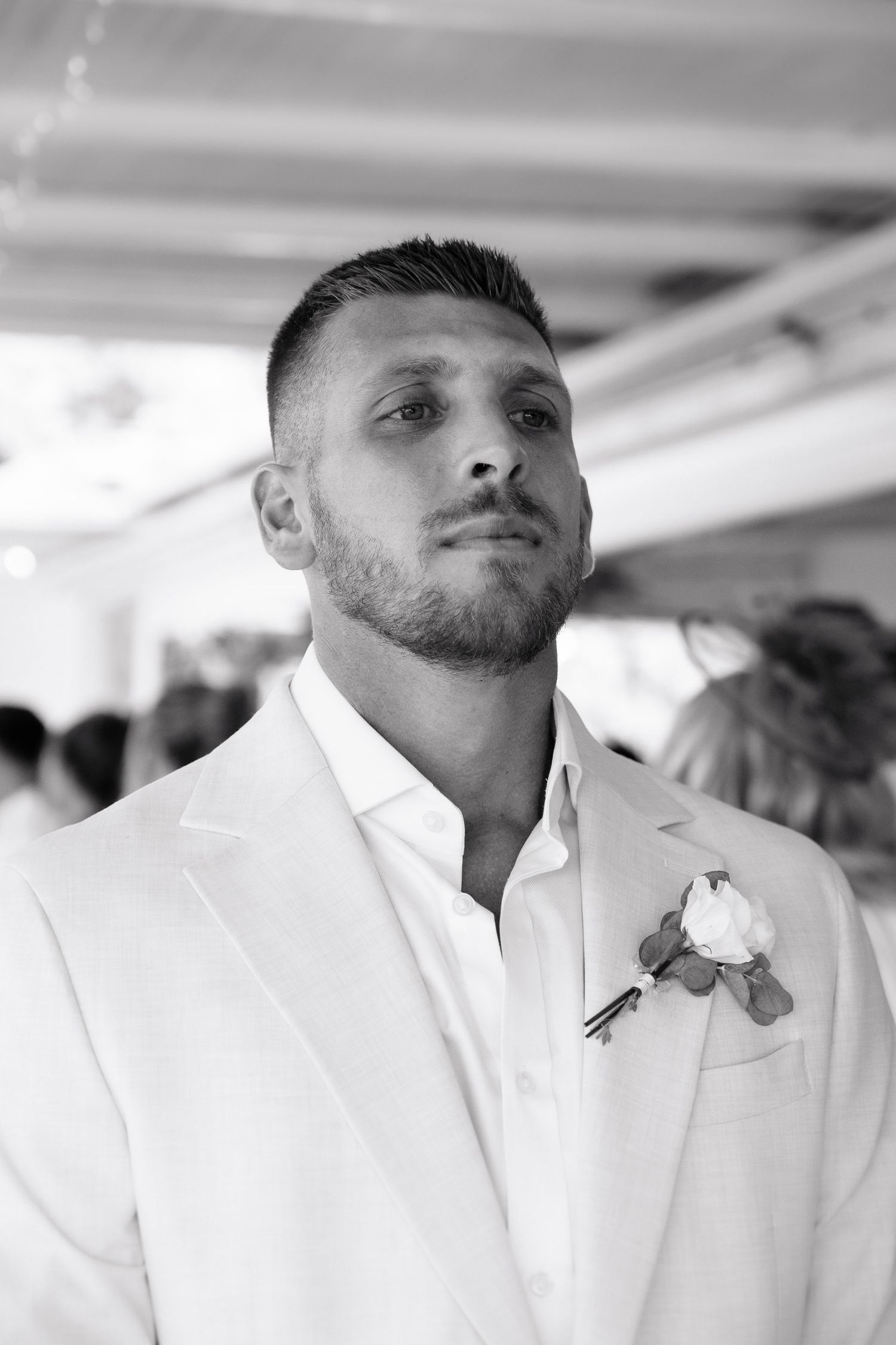 A person wearing a crisp white dress shirt with a boutonniere stands in an elegant indoor setting.