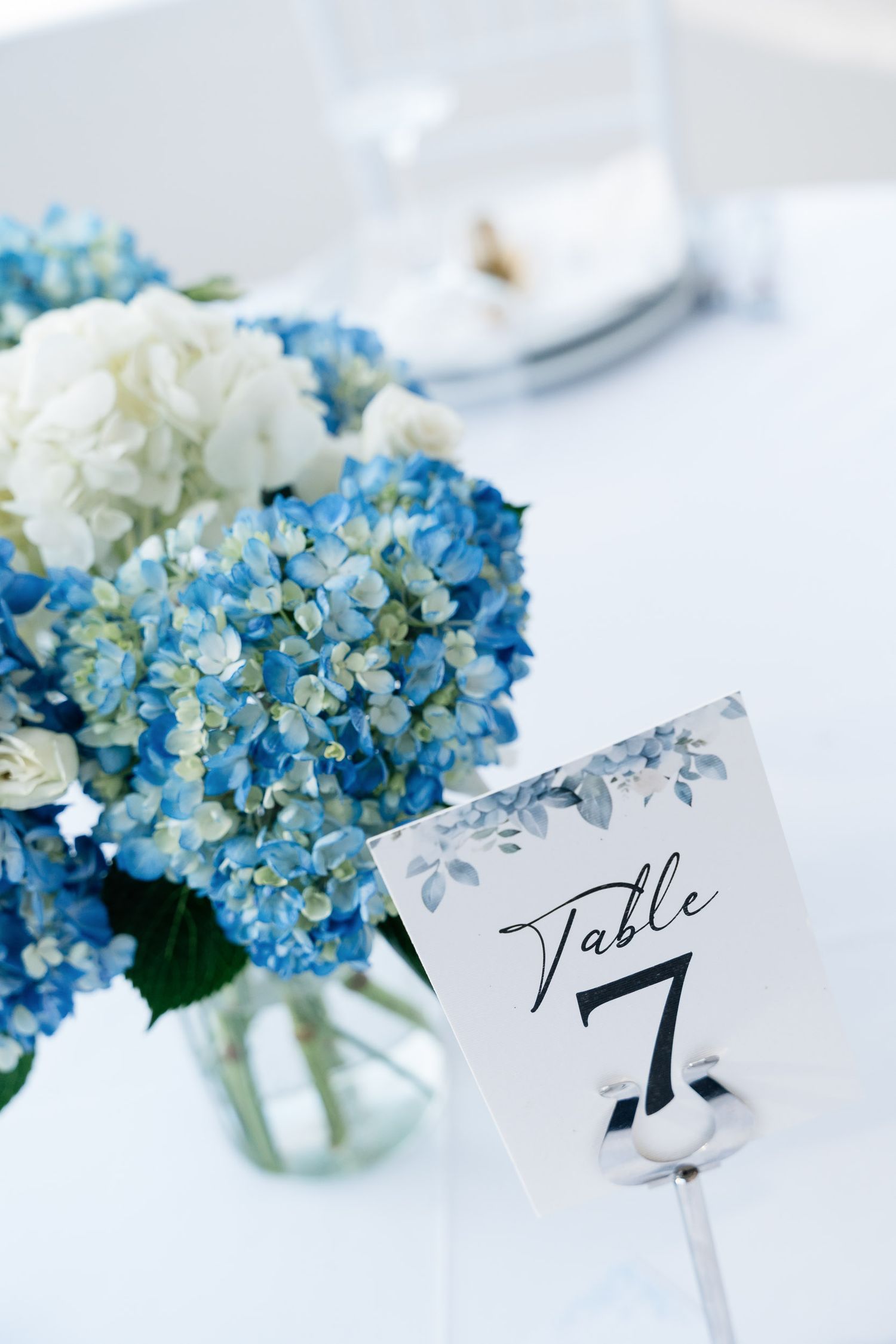 Blue and white hydrangea flowers in glass vases with elegant name place cards create a delicate table setting.