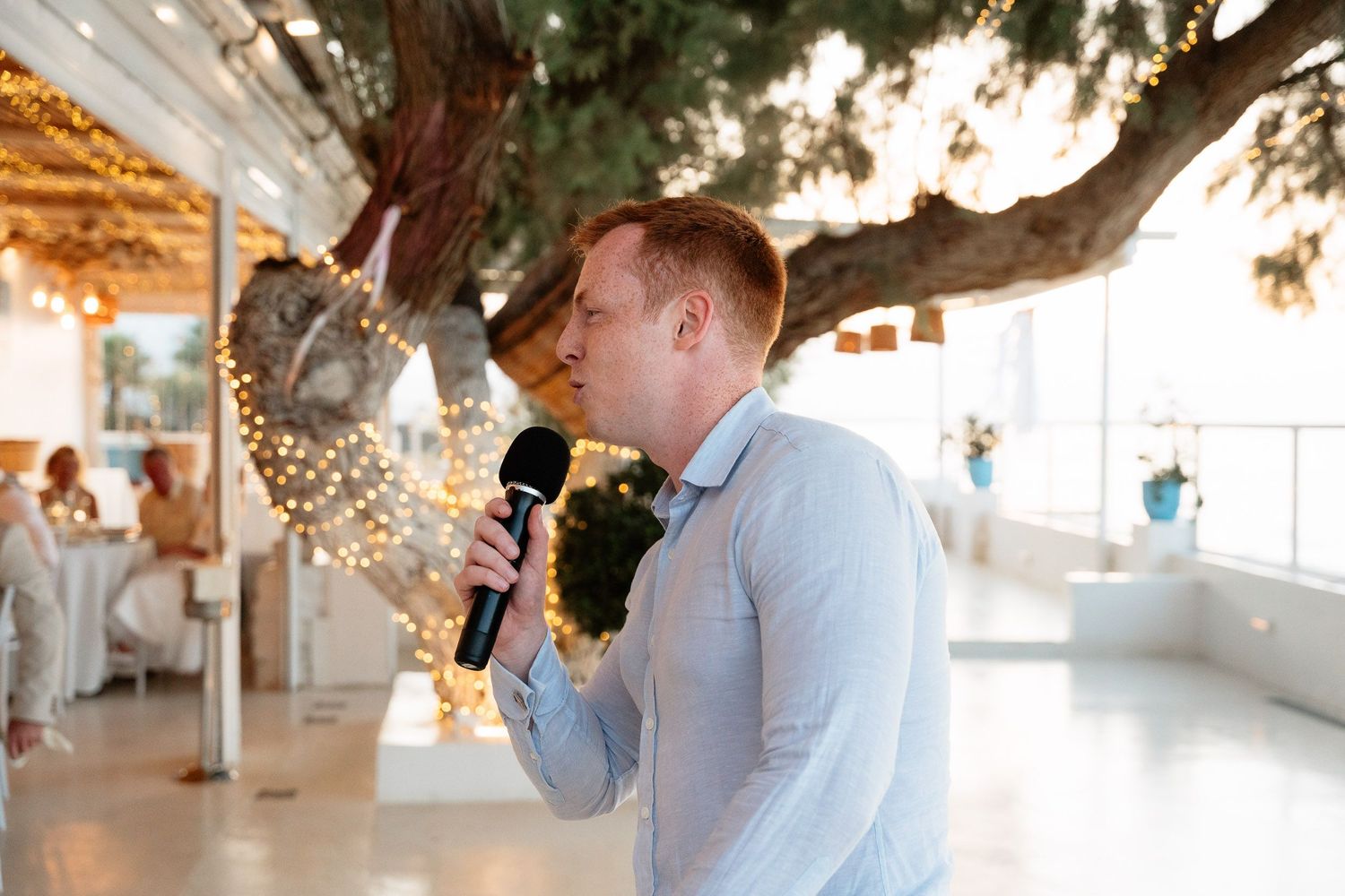 Wedding party members taking celebratory drinks under trees at an outdoor venue.