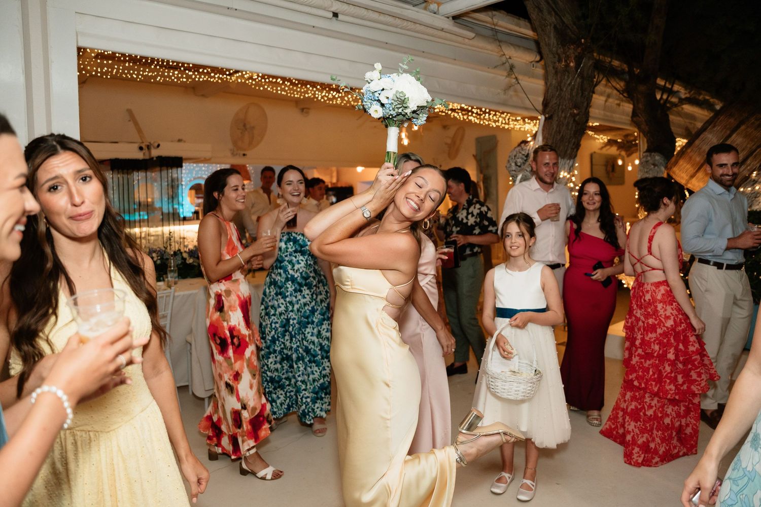 Wedding guests dance together on a reception dance floor with colorful dresses and festive lighting.