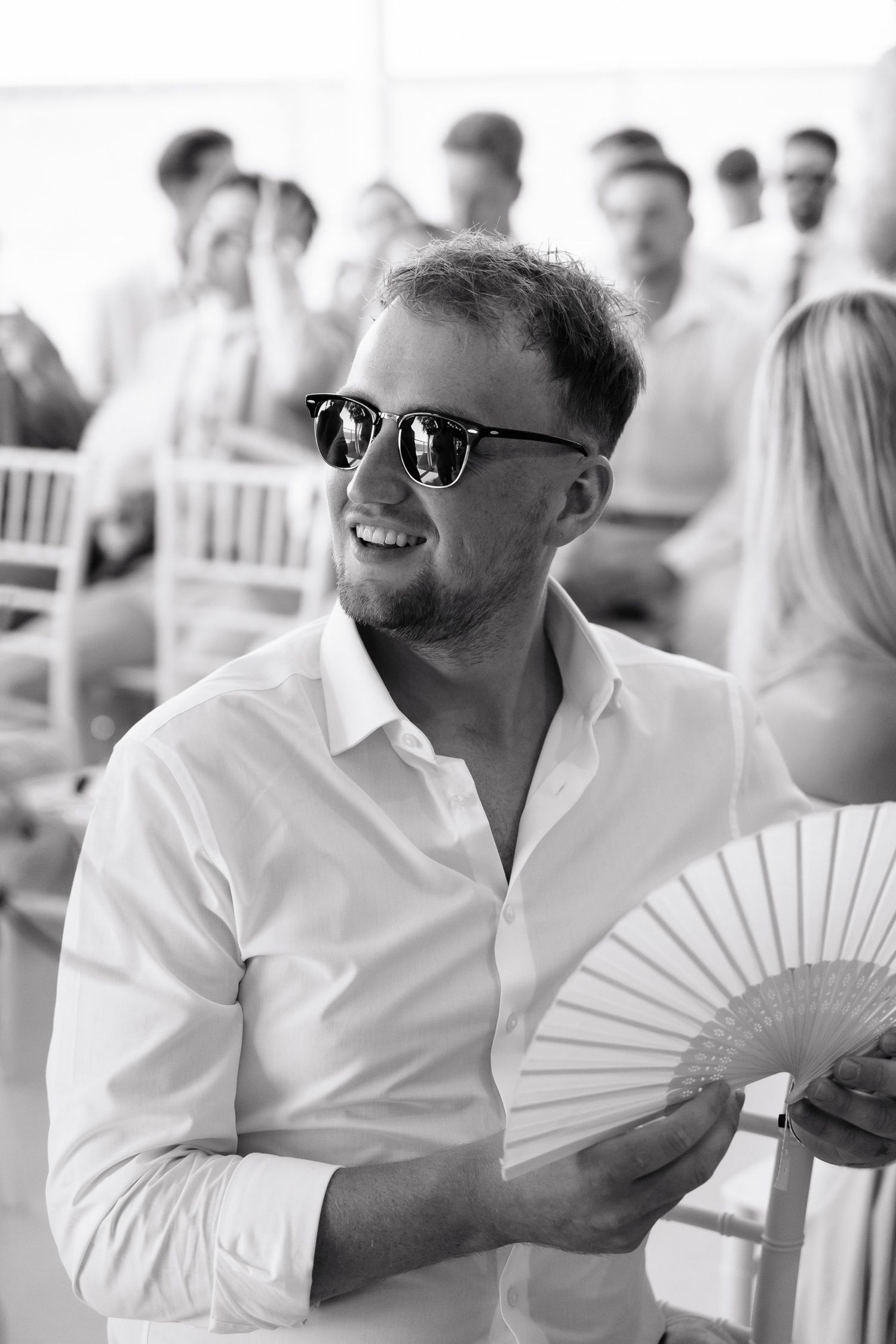 Three black and white photos show guests at an event wearing sunglasses and holding decorative white folding fans.