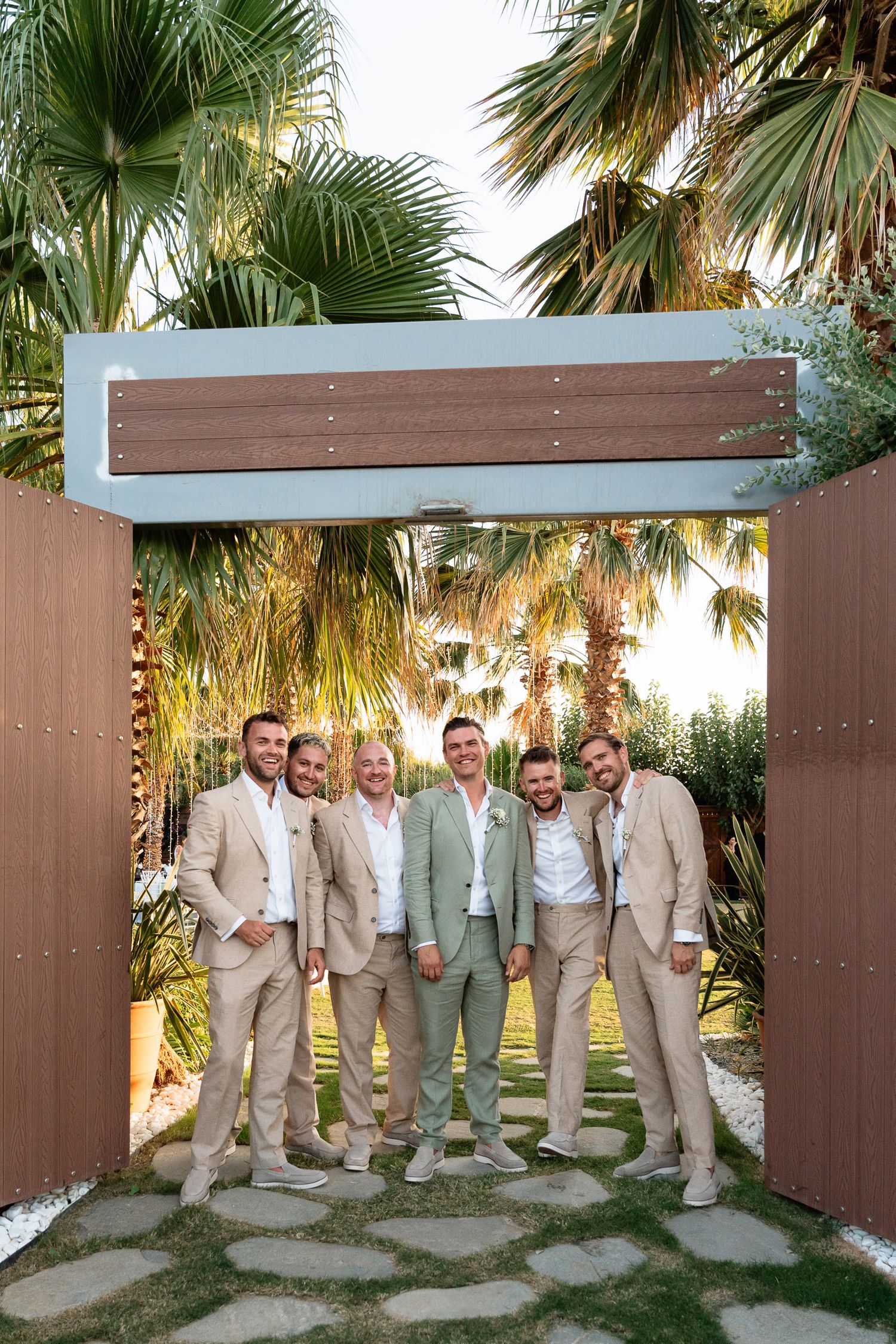 Groomsmen in khaki suits pose together in three similar shots against a tropical palm tree backdrop and wooden wall.