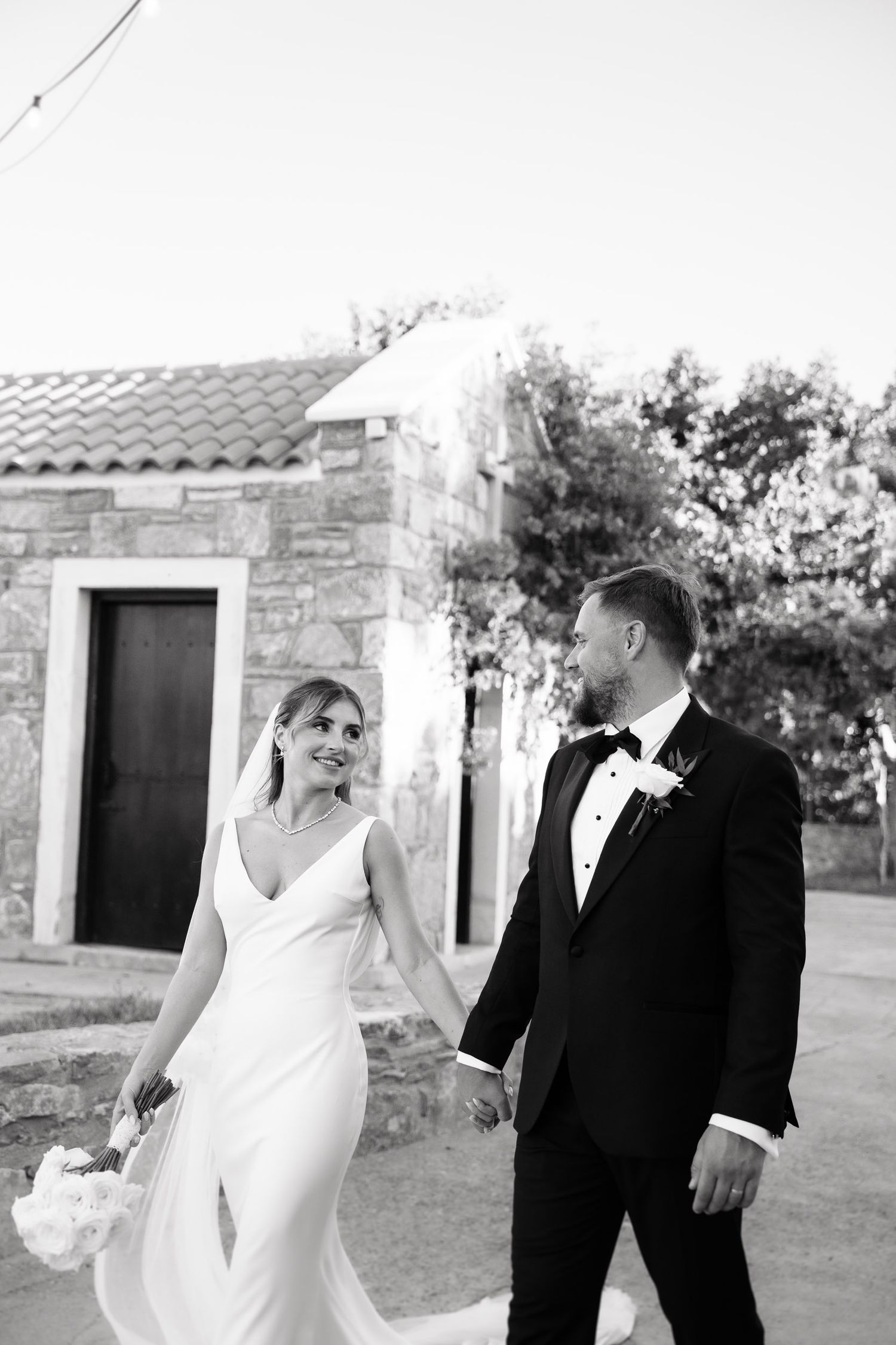 A couple shares a joyful candid moment together outdoors in black and white wedding attire.