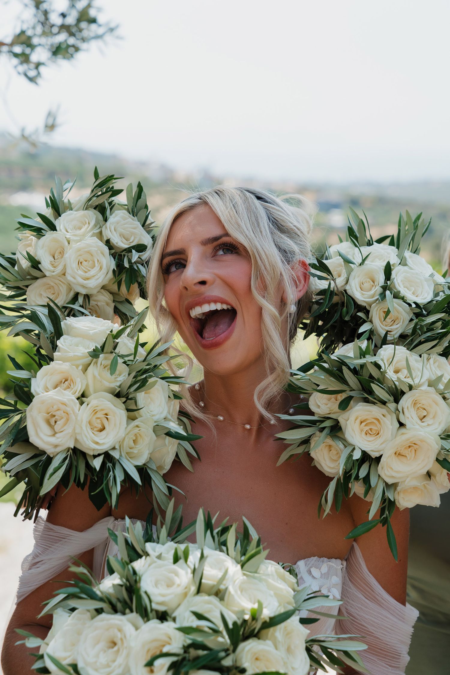 A stunning bridal bouquet featuring elegant white roses and lush green foliage against a scenic outdoor backdrop.