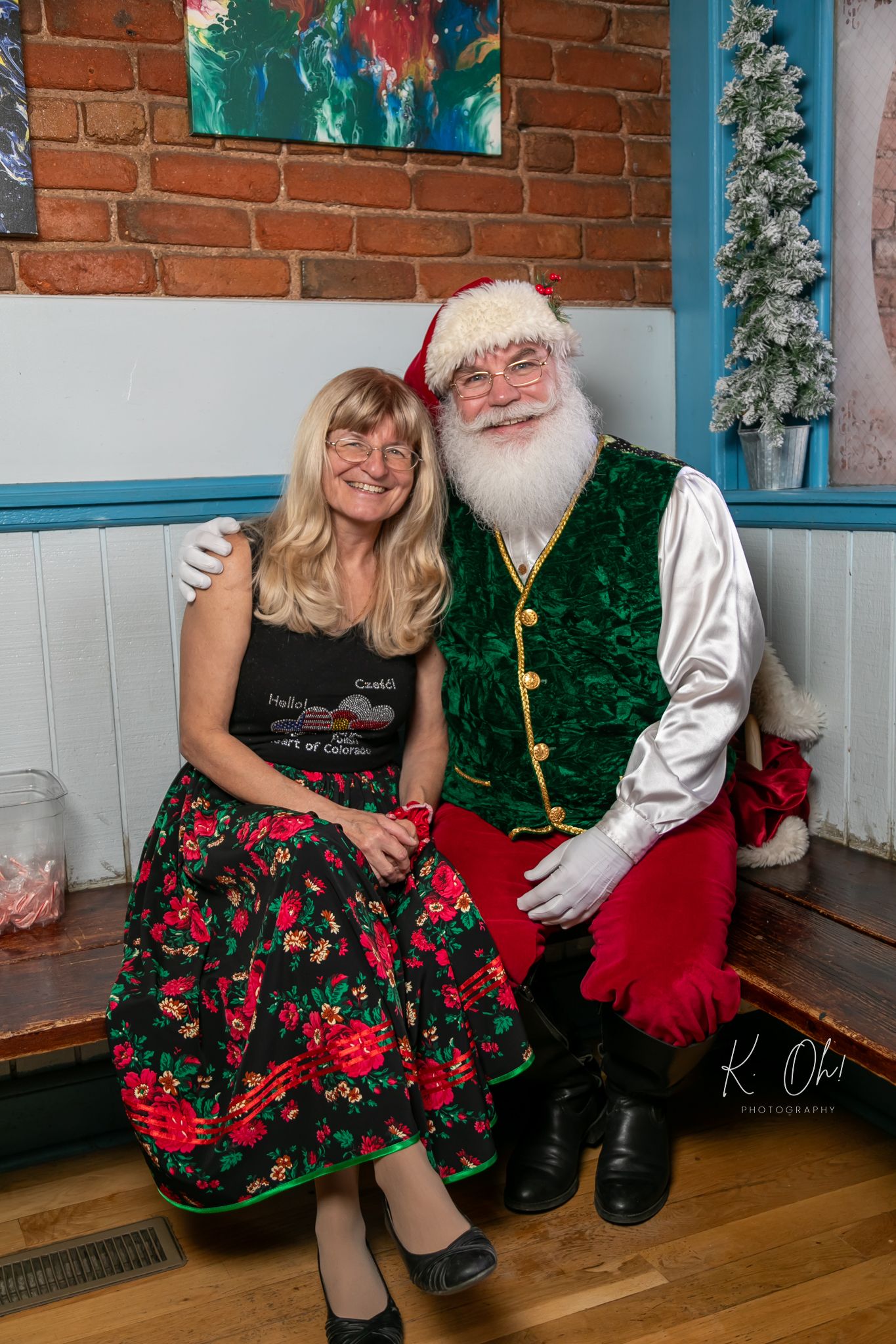 Holiday portrait with traditional Santa Claus figure and person in festive dress sitting together.