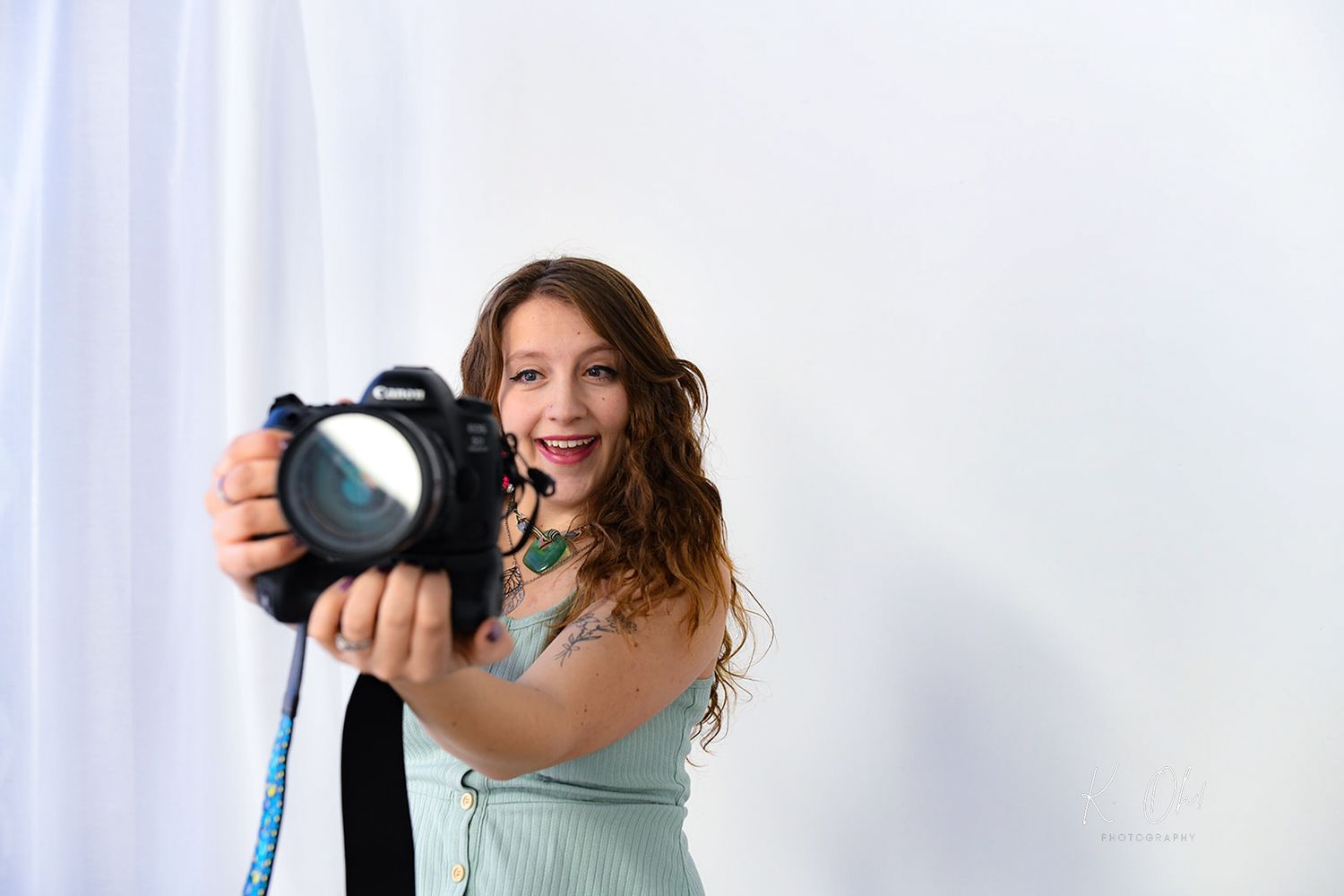 A photographer displays enthusiasm while holding professional camera equipment against a white backdrop.