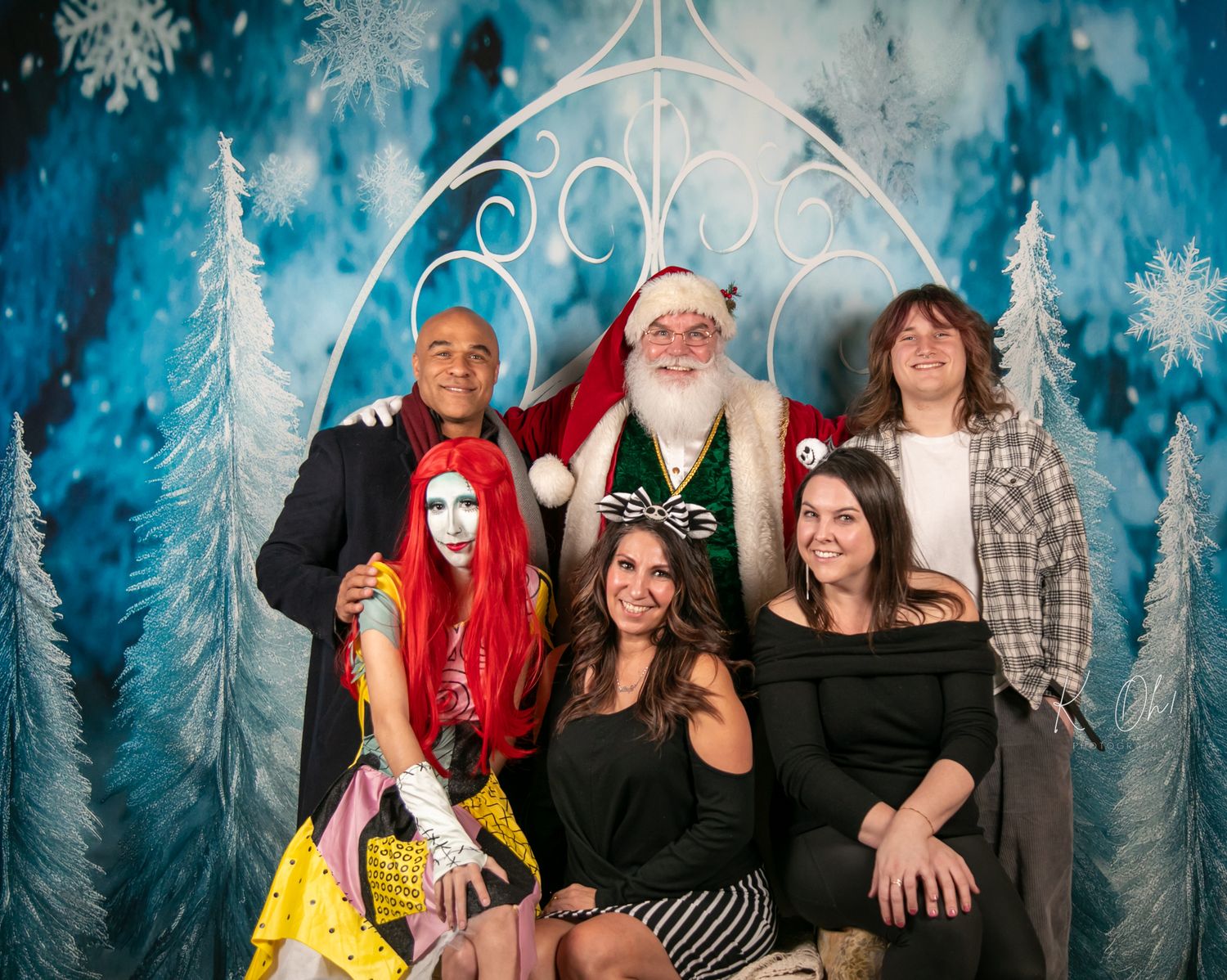 A group holiday photo in front of a winter backdrop with Santa Claus and decorative white trees.