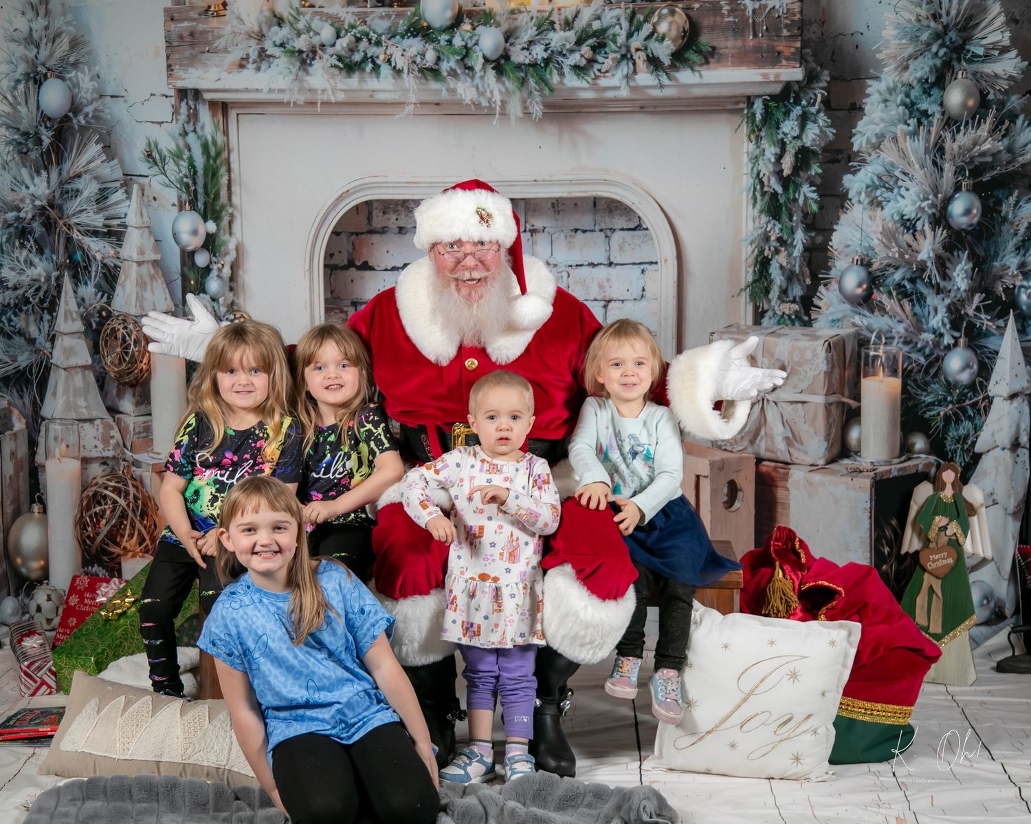 Santa Claus poses with young children in front of a decorated holiday fireplace setting.