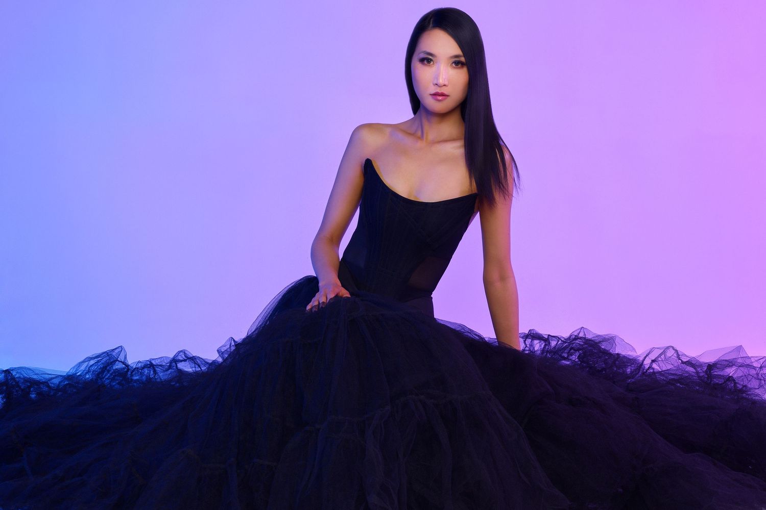 Black tulle ball gown worn against vibrant purple and blue gradient background.