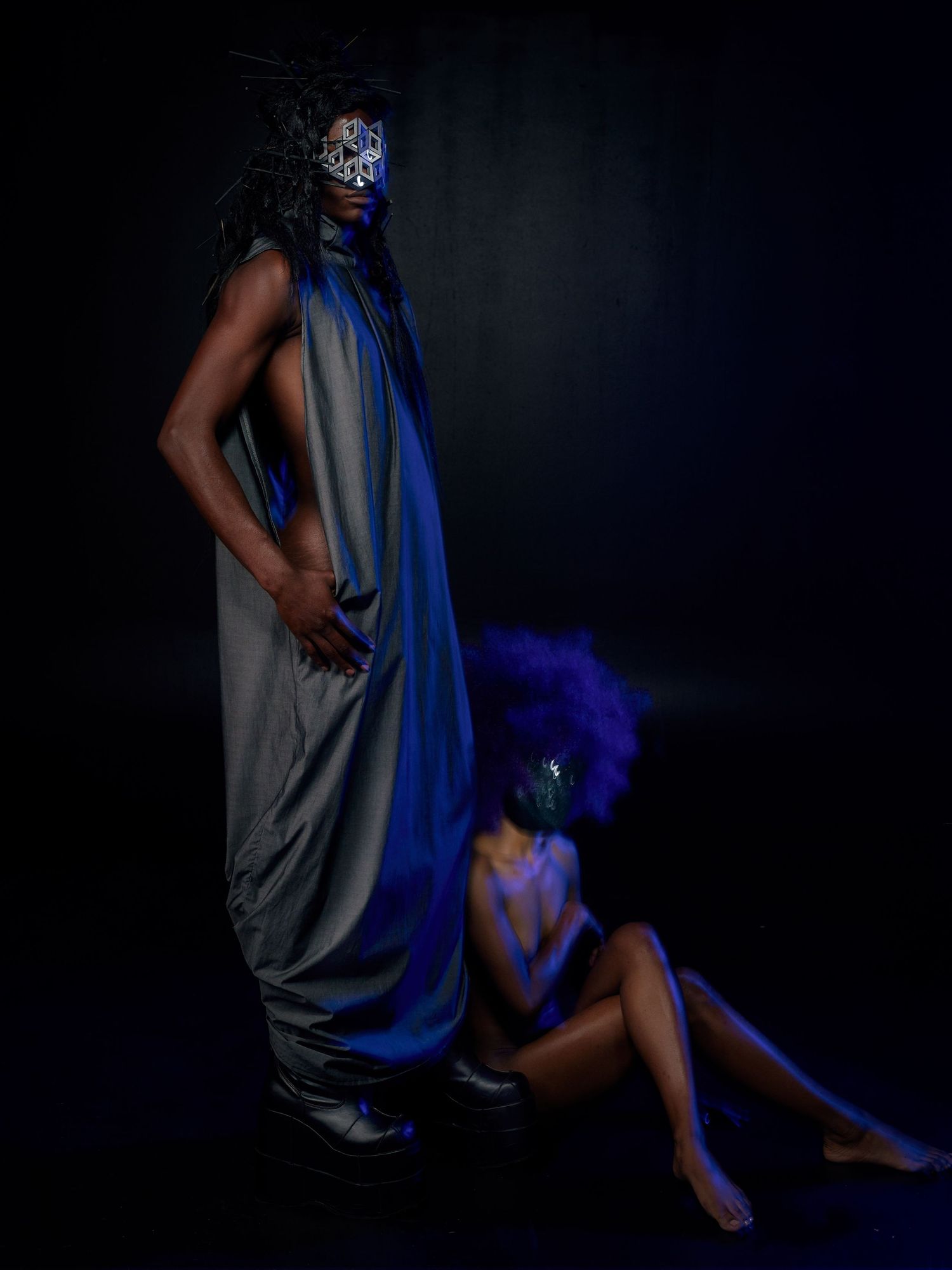 Artistic fashion portrait with dramatic blue draping and mask against dark background in moody studio lighting.