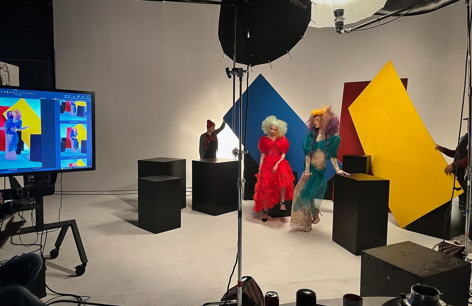 Professional video studio setup with colorful geometric backdrops, speakers, lighting equipment and a TV monitor display.