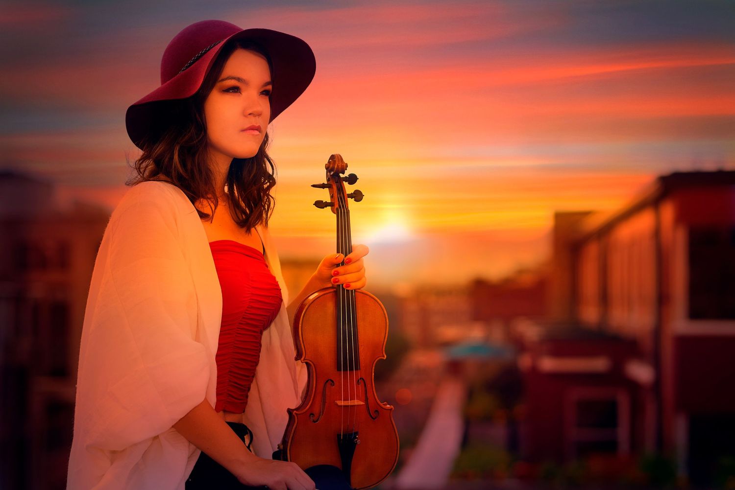 Musicians with violins perform against a dramatic orange and red sunset sky during a romantic evening photoshoot.