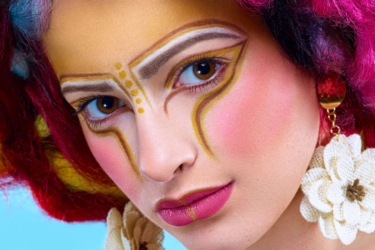 Creative beauty makeup with geometric gold lines and bold pink eyeshadow against turquoise background.
