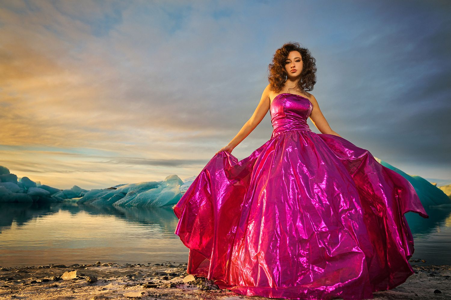 On Location fashion photography. A dramatic flowing magenta dress billows against a mountain landscape backdrop at sunset.