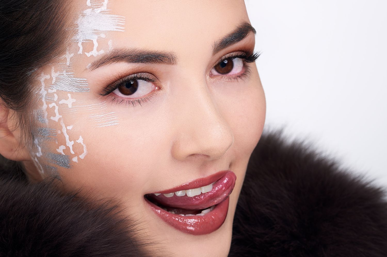 Beauty portrait with artistic white face paint decorations, glossy burgundy lipstick and black fur collar.