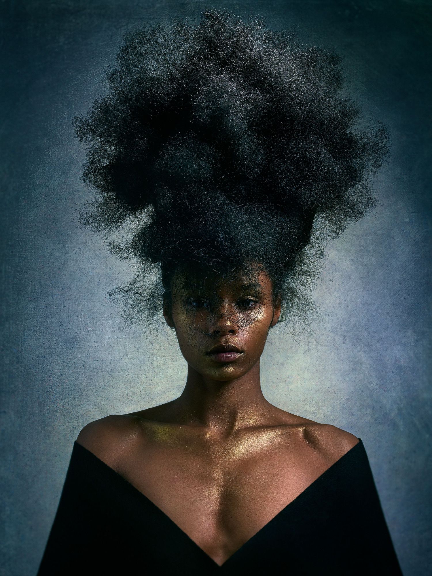 Striking artistic portrait of a model wearing black against dramatic lighting with natural hair styled upward dramatically.