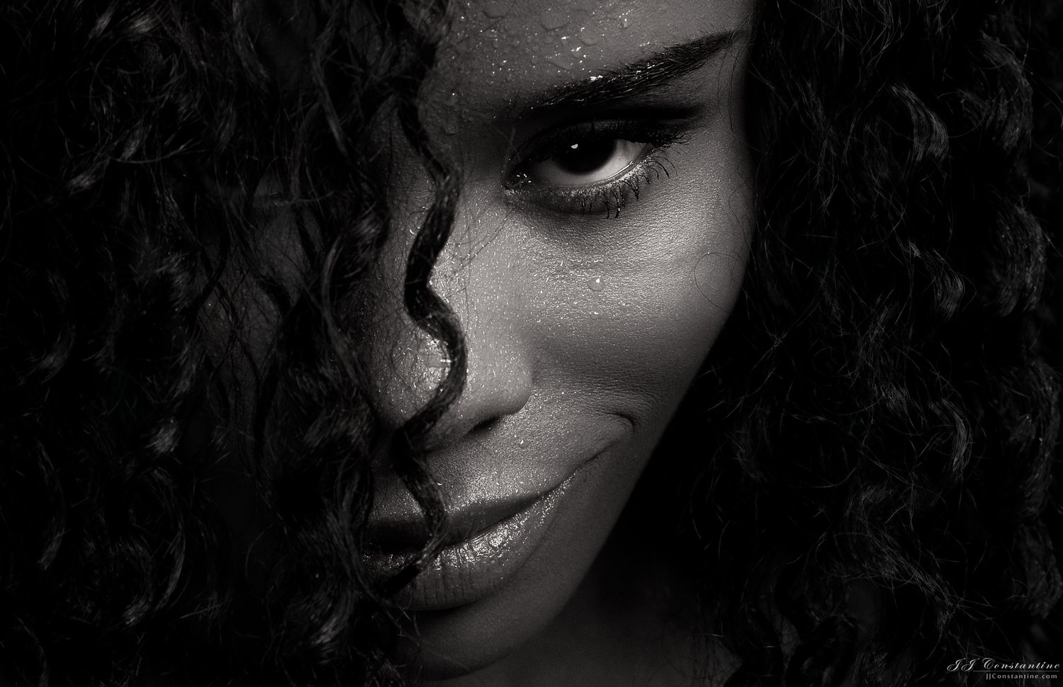Dramatic black and white close-up portrait showcasing curly hair and striking features in moody lighting. — fine art photography Denver.