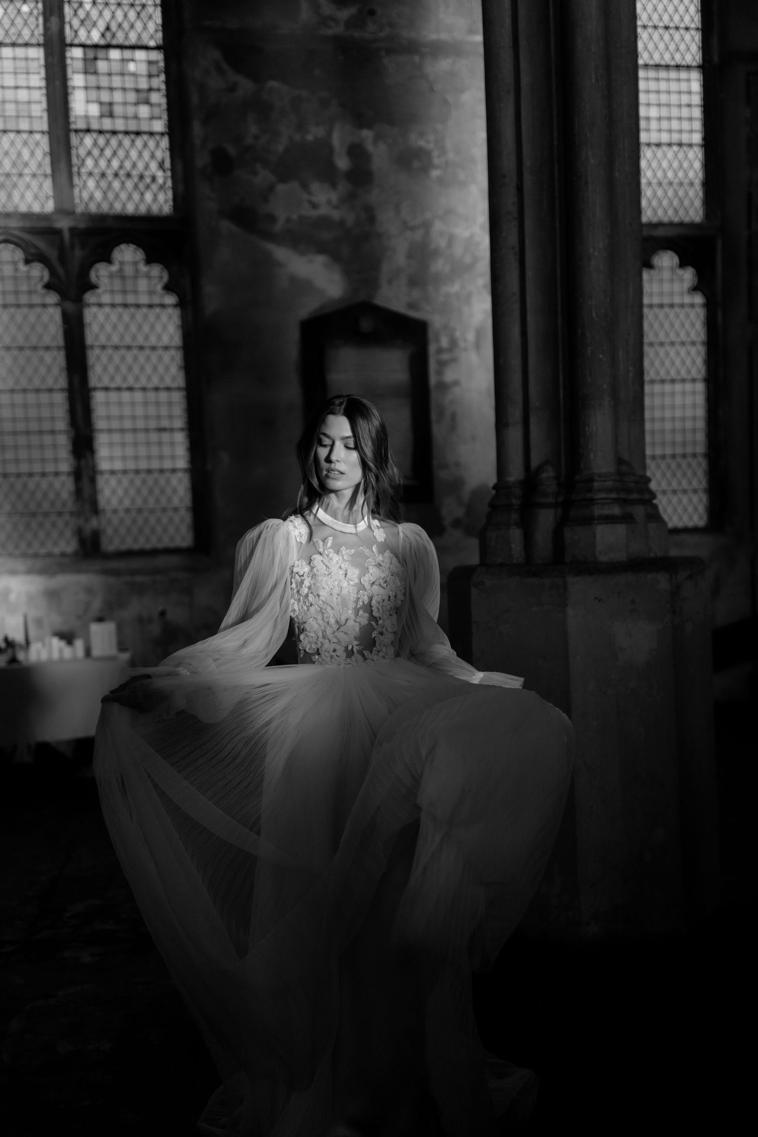 Black and white photo of a bride in a flowing lace gown standing in a grand historic church interior.