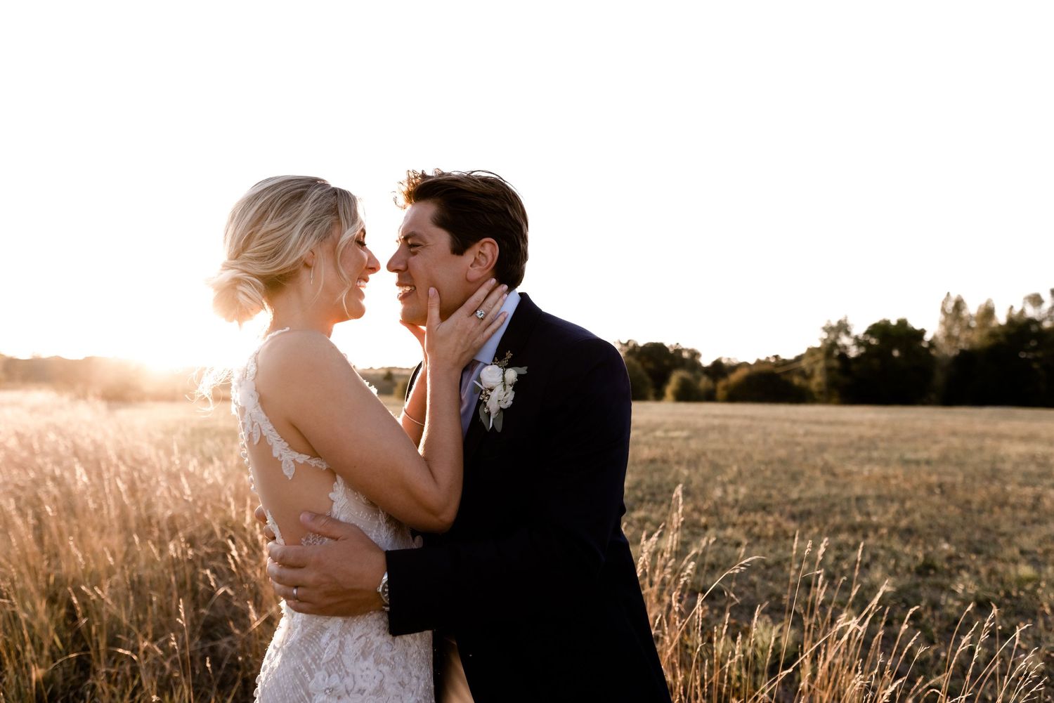Wedding couple embracing in golden sunlit field during sunset photo session.