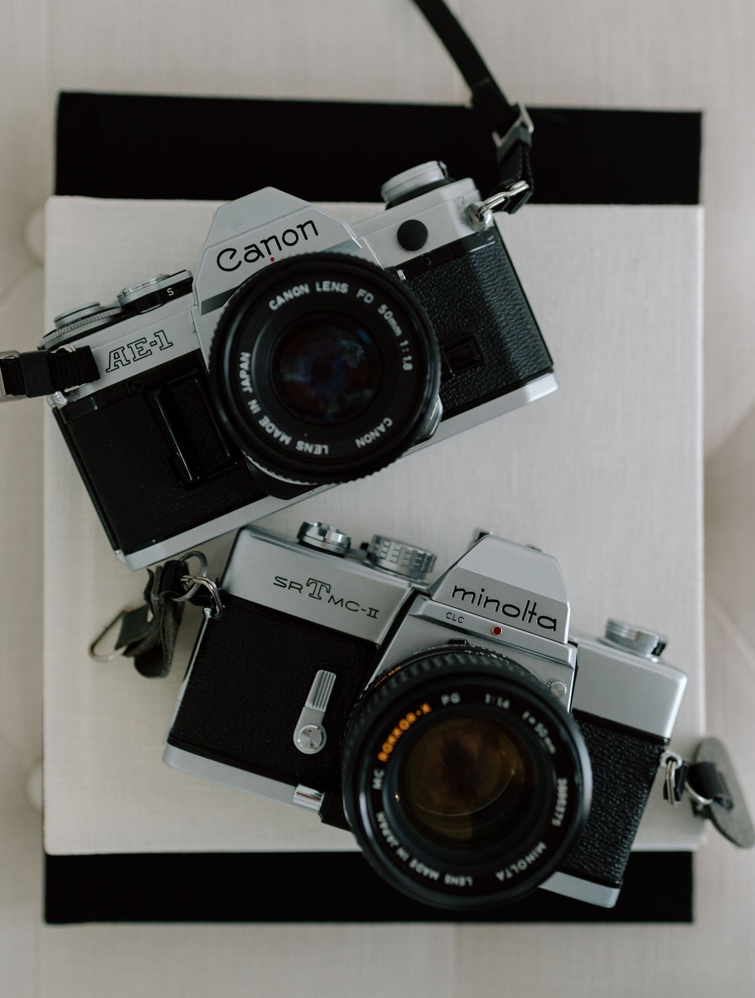 Two vintage film cameras, a Canon and a Minolta SRT, arranged on black and white background.