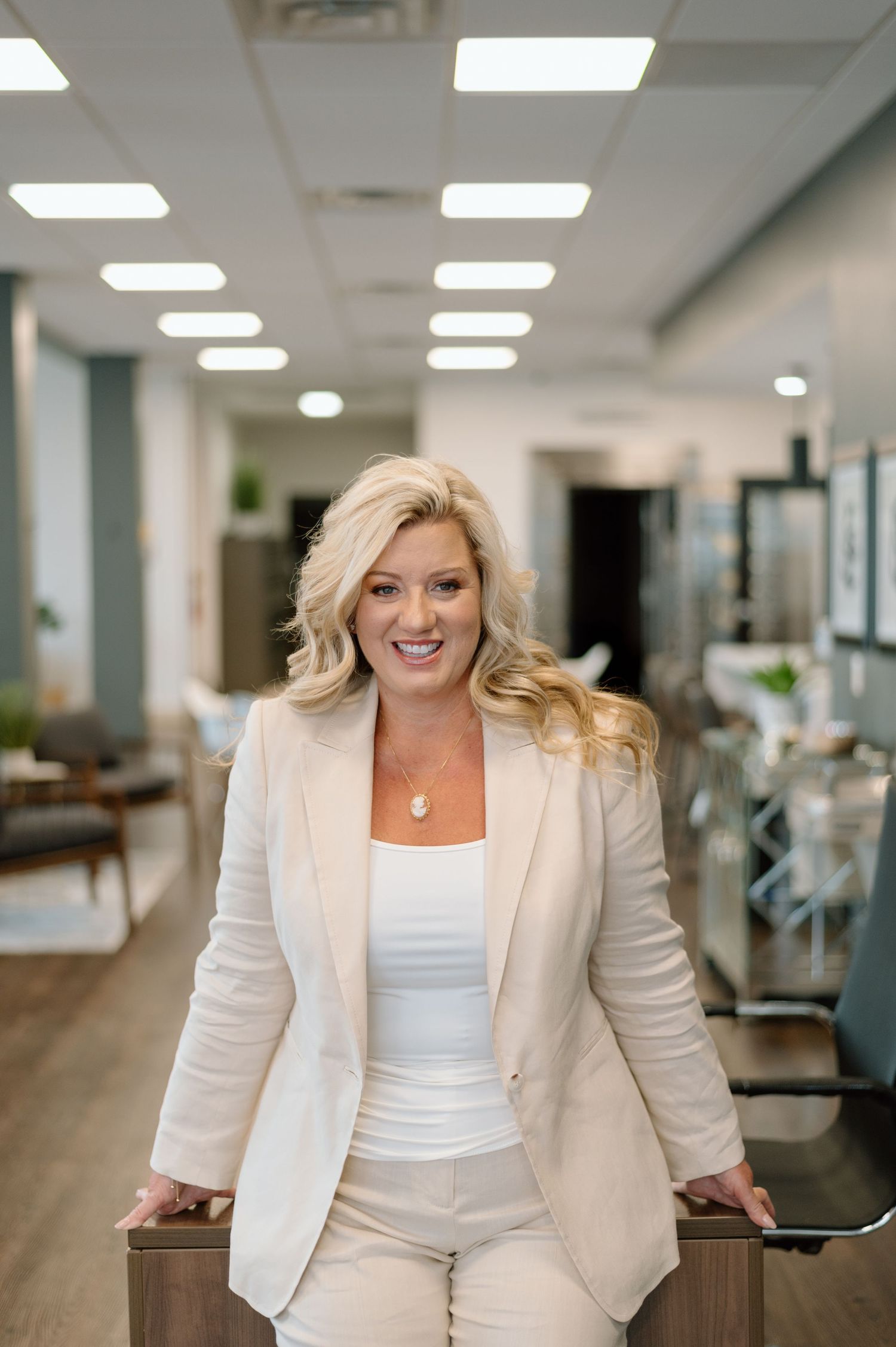 Professional woman in all-white business attire stands confidently in a modern office hallway with recessed lighting.
