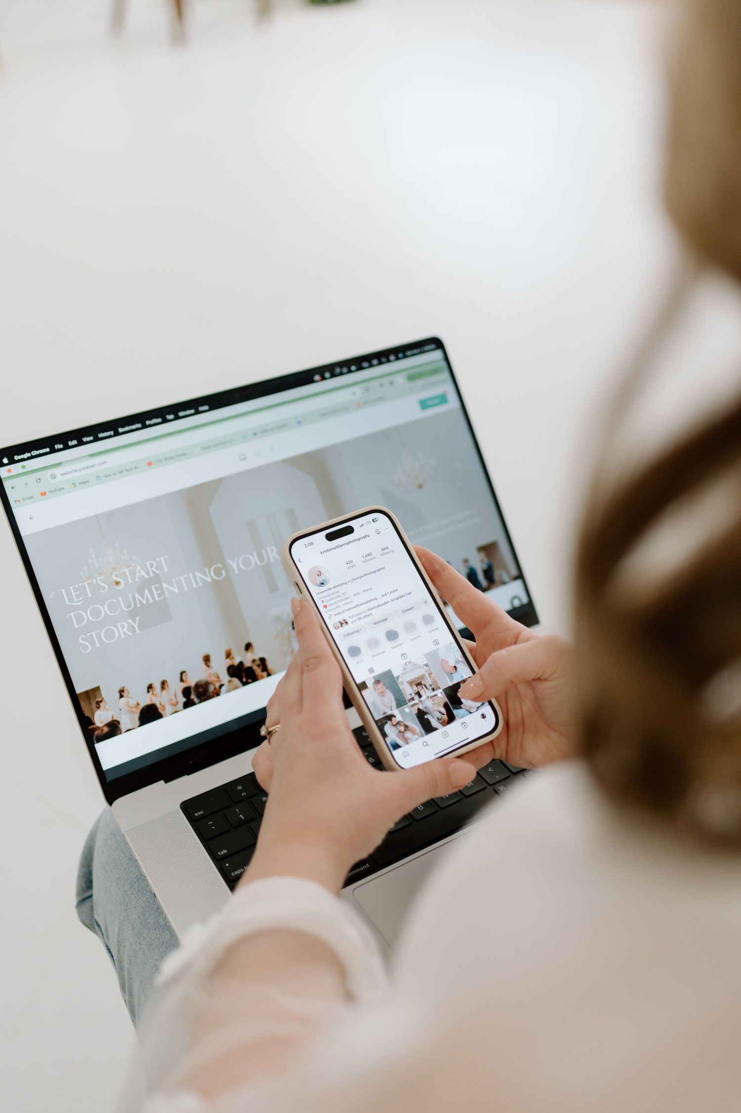 Person holding iPhone while viewing synchronized content on laptop screen showing minimalist website design.