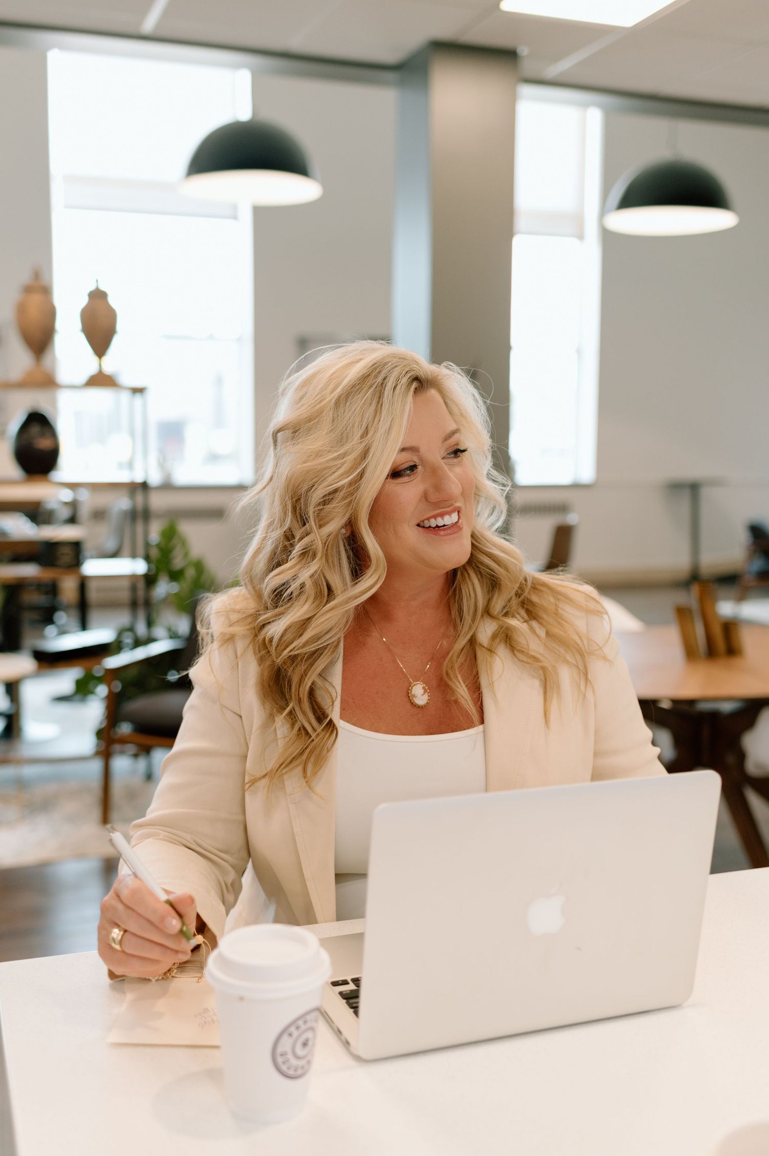 Professional working on laptop at modern coworking space with industrial pendant lamps and minimalist decor.