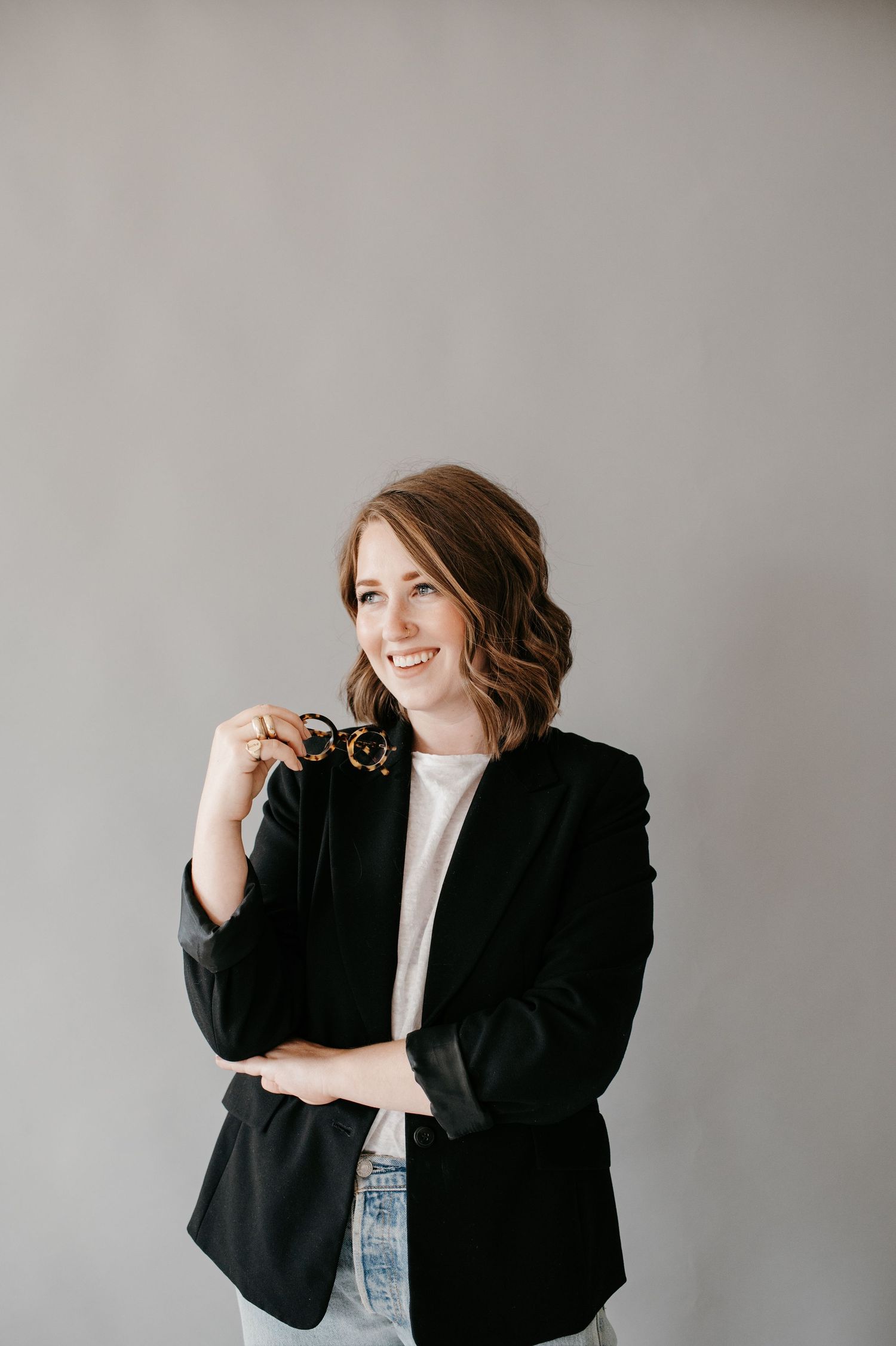 Professional portrait of someone wearing a black blazer and white top against a gray background, smiling warmly.